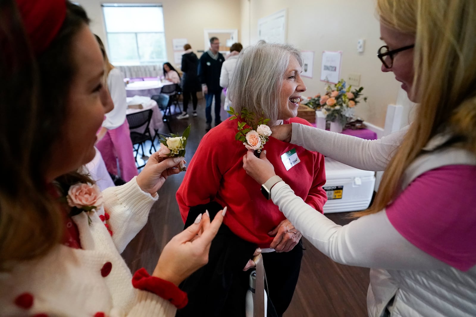 Jillian Myers, left, looks on as Ashley Manning, right, places a boutonniere on widow Linda Thompson, in honor of her husband, during a Valentine's Day Widow Outreach Project event, Thursday, Feb. 13, 2025, in Charlotte, N.C. (AP Photo/Erik Verduzco)