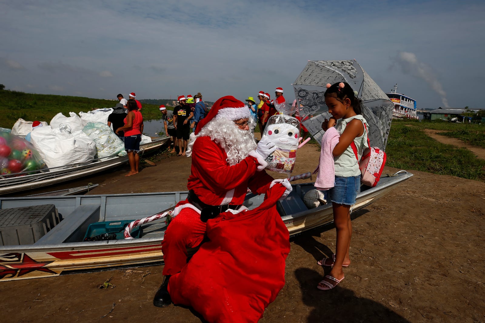 Jorge Barroso, dressed as Santa Claus, presents a gift to a young resident after arriving on a boat to distribute Christmas gifts to children who live in the riverside communities of the Amazon, in Iranduba, Brazil, Saturday, Dec. 21, 2024. (AP Photo/Edmar Barros)