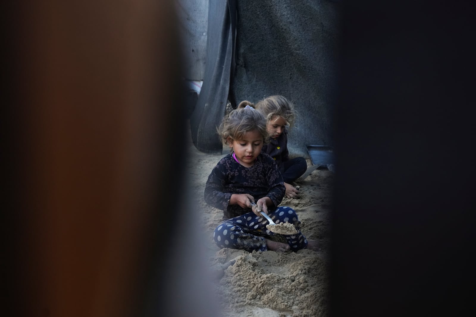 Grandchildren of Reda Abu Zarada, displaced from Jabaliya in northern Gaza, play with sand next to their tent at a camp in Khan Younis, Gaza Strip, Thursday, Dec. 19, 2024. (AP Photo/Abdel Kareem Hana)