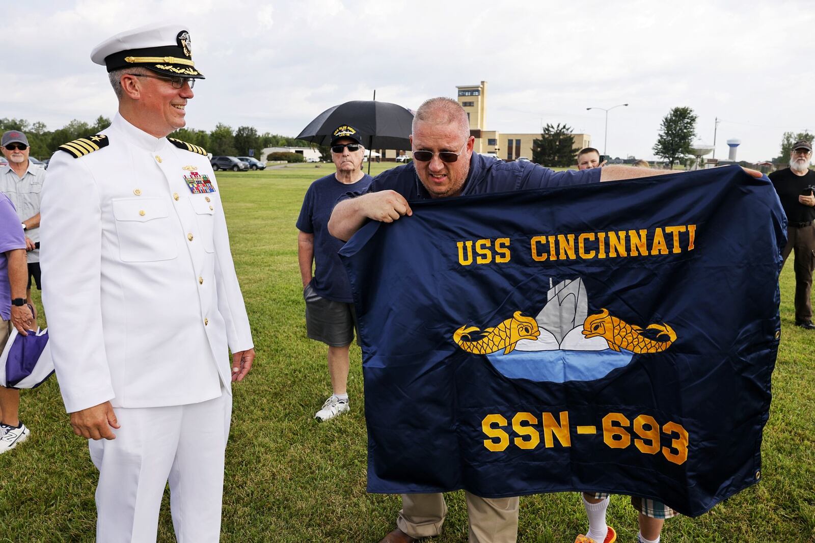 U.S. Navy Cpt. Jeff Lamphear looks a flag held by Kevin McDaniels, who served on the USS Cincinnati, during a groundbreaking ceremony held Wednesday, July 31, 2024 for the USS Cincinnati Memorial and Peace Pavillion between Voice of America Park and The National Voice of America Museum of Broadcasting in West Chester Township. NICK GRAHAM/STAFF