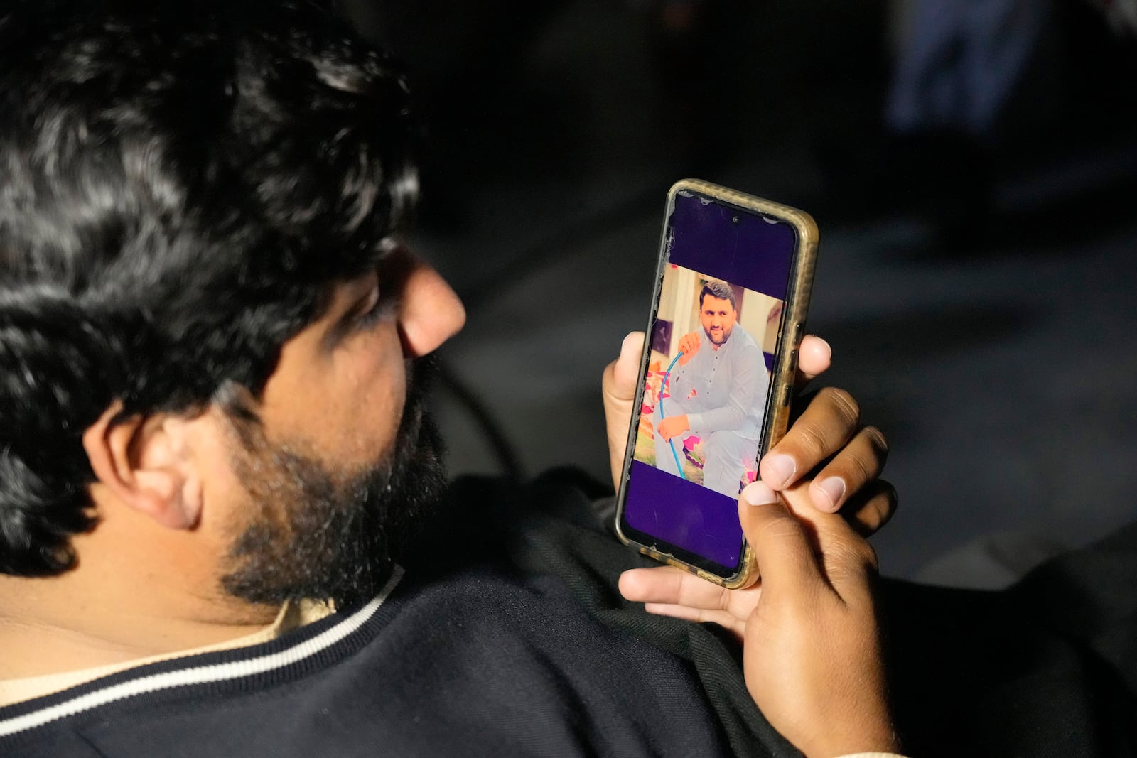 Ahsan Shahzad, shows a picture of his son, Suffian Ali, one of the victims of a migrant boat that capsized in West Africa's Atlantic coastline, on his cell phone at his home in the village of Dhola, Lalamusa district, Pakistan, Friday, Jan. 17, 2024. (AP Photo/K.M. Chaudary)