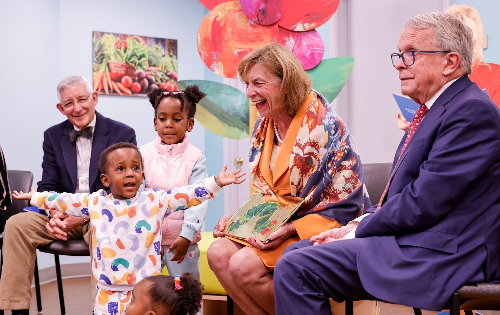 Marcus Johnson, 2, and Marcia Johnson, 4, pretend to be butterflies during a visit by Ohio Gov. Mike DeWine and first lady Fran DeWine at a Butler County WIC office to read a book to kids and promote a new children's reading kiosk Monday, Oct. 28, 2024, in downtown Hamilton. Ten reading kiosks, developed by the Ohio Department of Health and Dolly Parton's Imagination Library, are being installed at WIC offices around the state to be used by families visiting the clinics. At left is Dr. Bruce Vanderhoff, the state's health director. NICK GRAHAM/STAFF