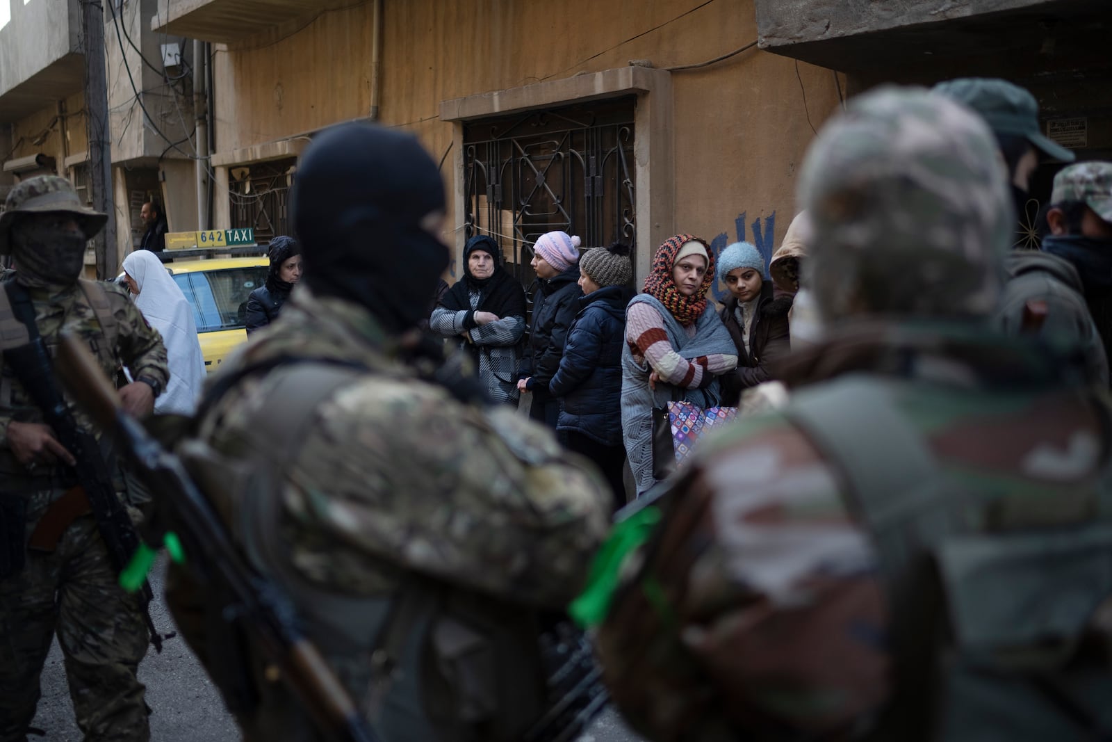 People stand outside their homes at a residential area as members of the new security forces take part in an operation to detain, according to the state media, militiamen affiliated with ousted president Bashar Assad in Homs, Syria, Thursday, Jan. 2, 2025. (AP Photo/Leo Correa)