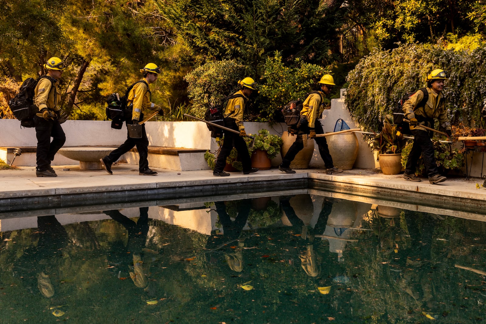 A Cal Fire hand crew walks past a swimming pool toward their next assignment during the Palisades Fire in the Mandeville Canyon neighborhood of Los Angeles, Calif., Saturday, Jan. 11, 2025. (Stephen Lam/San Francisco Chronicle via AP)