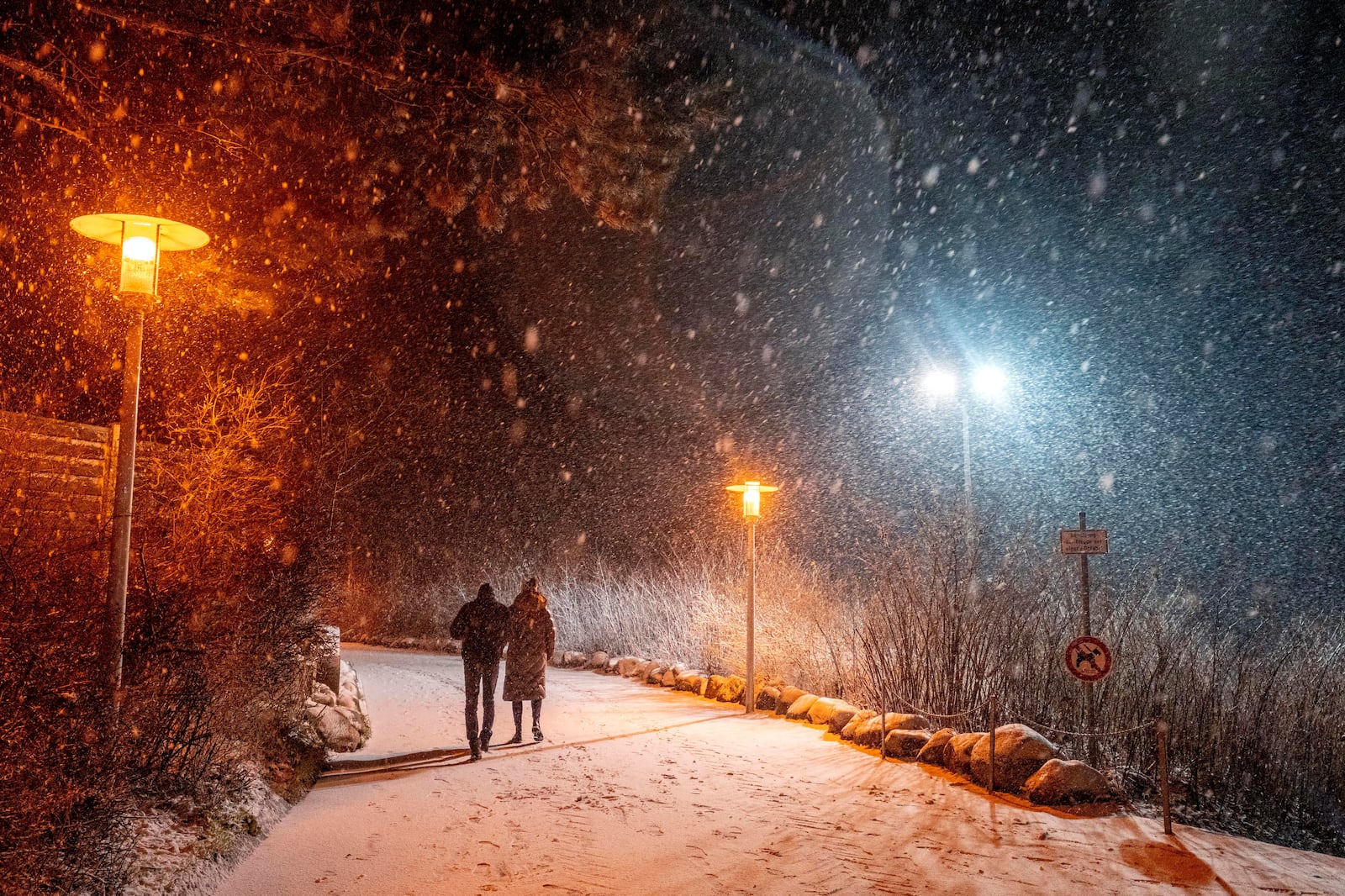 People stroll on the beach at the Baltic Sea in Timmendorfer Strand, Germany, during heavy snowfalls on Sunday, Jan. 5, 2025. (AP Photo/Michael Probst)