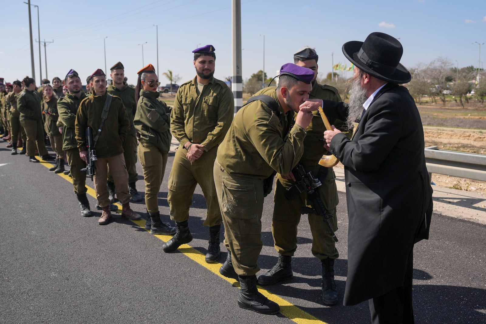 An Israeli soldier kisses the hand of an ultra-Orthodox Jewish man while they are waiting on the side of a road where the funeral convoy carrying the coffins of slain hostages Shiri Bibas and her two children, Ariel and Kfir, will pass by near Kibbutz Nir Oz, Israel, Wednesday, Feb. 26, 2025. The mother and her two children were abducted by Hamas on Oct. 7, 2023, and their remains were returned from Gaza to Israel last week as part of a ceasefire agreement with Hamas. (AP Photo/Ohad Zwigenberg)