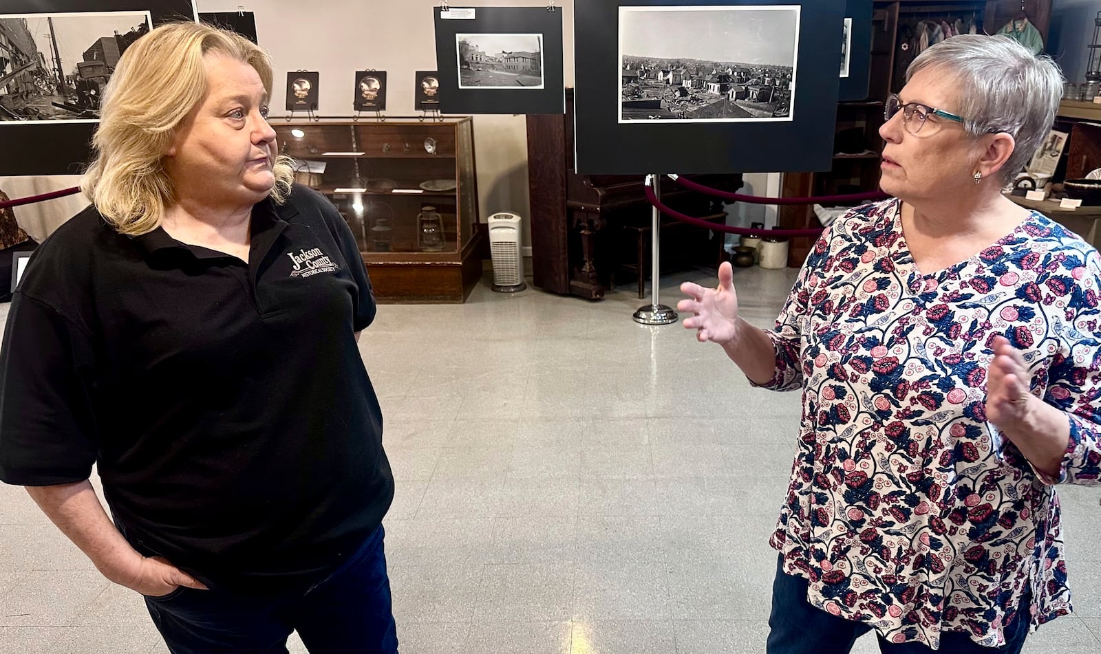 Jackson County Historical Society President Laura Cates Duncan, right, and Mary Riseling, a society board member and coordinator of the 100th anniversary commemoration of the Tri-State Tornado, discuss the March 18, 1925 cataclysm while standing among a gallery of photos on display at the society's office on March 11, 2025 in Murphysboro, Ill. (AP Photo/John O'Connor)