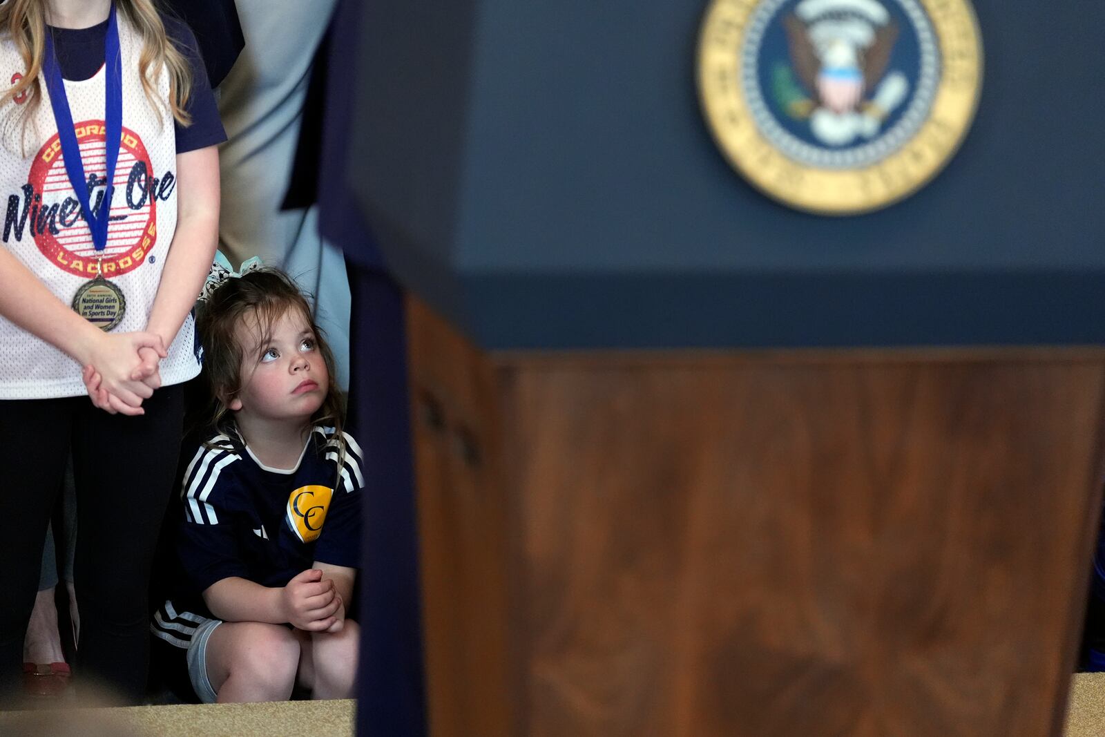 A young girl watches as President Donald Trump speaks before signing an executive order barring transgender female athletes from competing in women's or girls' sporting events, in the East Room of the White House, Wednesday, Feb. 5, 2025, in Washington. (AP Photo/Alex Brandon)