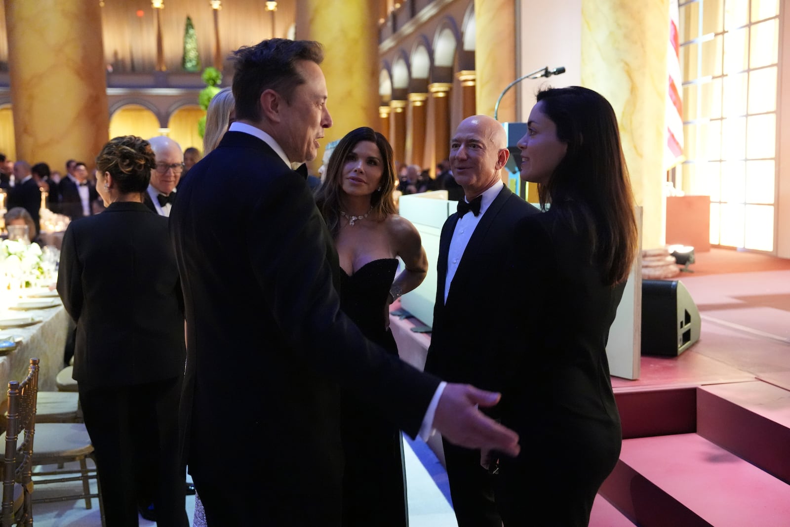 Elon Musk talks guests including Jeff Bezos and his wife MacKenzie Scott, third from right, before President-elect Donald Trump speaks at a dinner at the Building Museum, Sunday, Jan. 19, 2025, in Washington. (AP Photo/Evan Vucci)