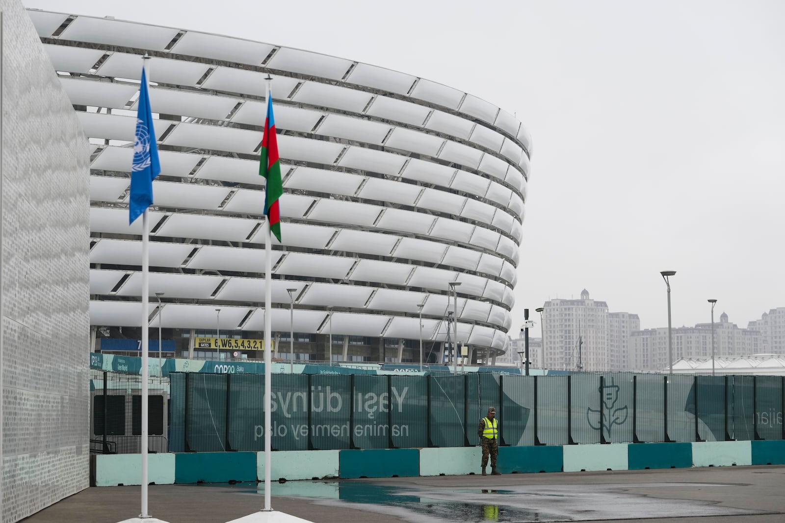 A member of security stands with the Baku Olympic Stadium in the background during the COP29 U.N. Climate Summit, Saturday, Nov. 23, 2024, in Baku, Azerbaijan. (AP Photo/Sergei Grits)