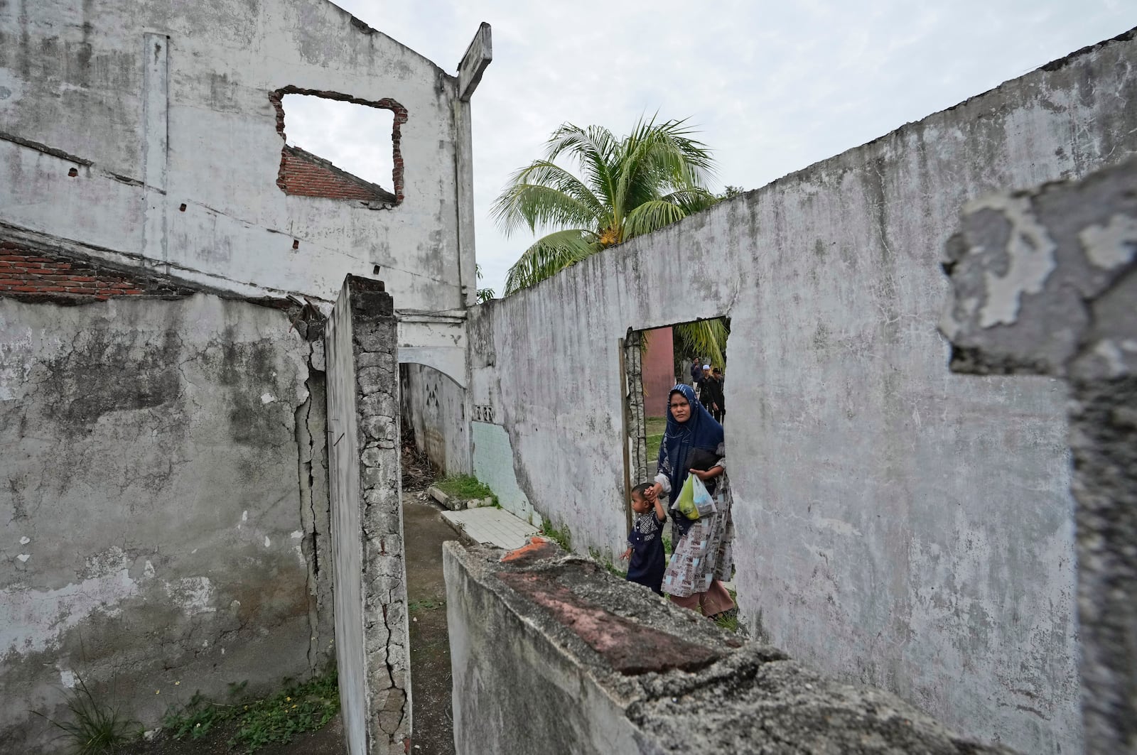 A woman walks trough an opening on the wall of a building badly damaged during the Indian Ocean tsunami in 2004 in Banda Aceh, Aceh province, Indonesia, Saturday, Dec 14, 2024. (AP Photo/Achmad Ibrahim)