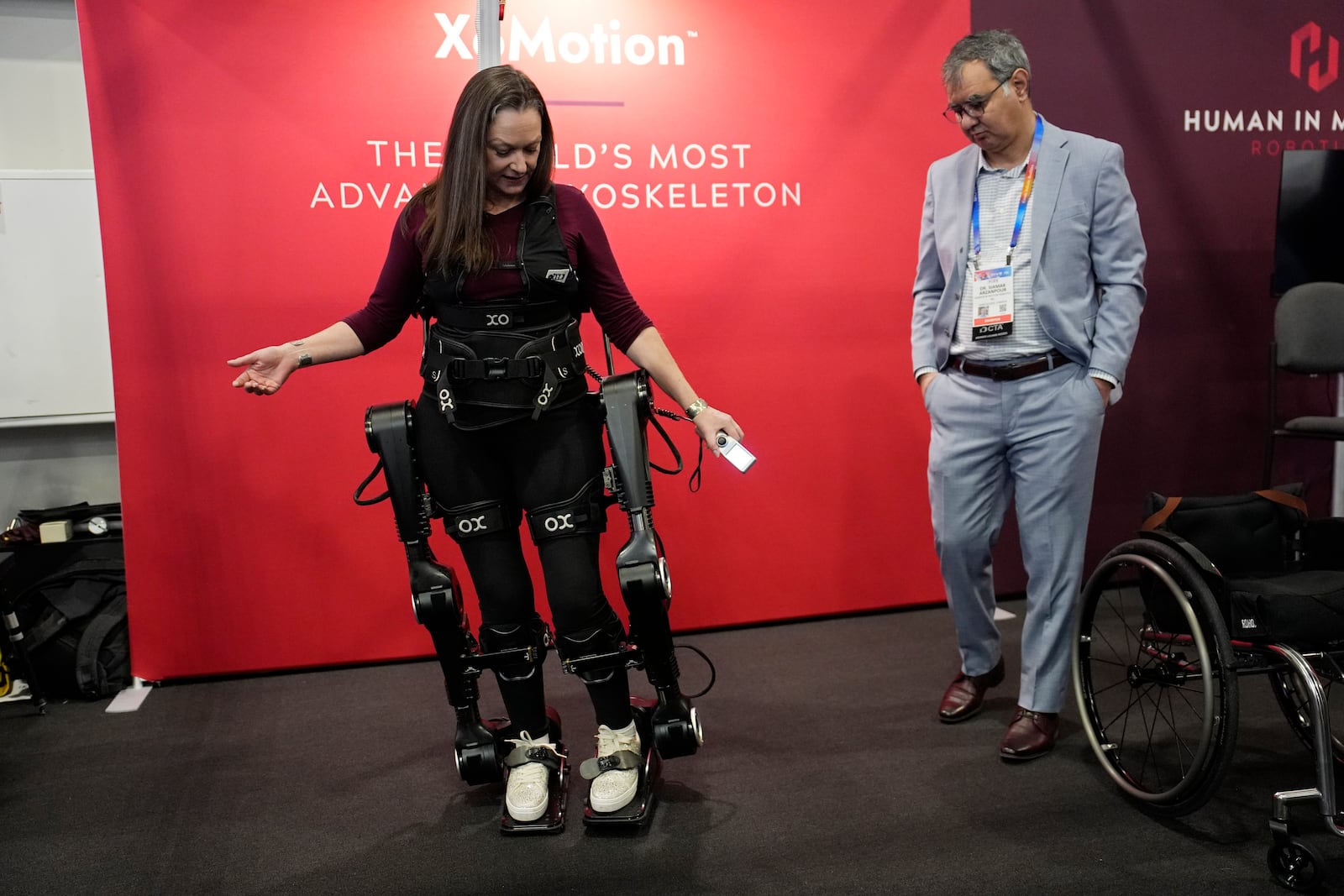 Chloe Angus, director of Lived Experience at Human in Motion Robotics and paraplegic, stands and moves with help from the XoMotion exoskeleton at the Human In Motion Robotics booth during the CES tech show Wednesday, Jan. 8, 2025, in Las Vegas. The wearable robotic exoskeleton is designed to assist patients with mobility impairments due to spinal cord injuries, stroke and other neurological conditions in standing up and walking. (AP Photo/John Locher)