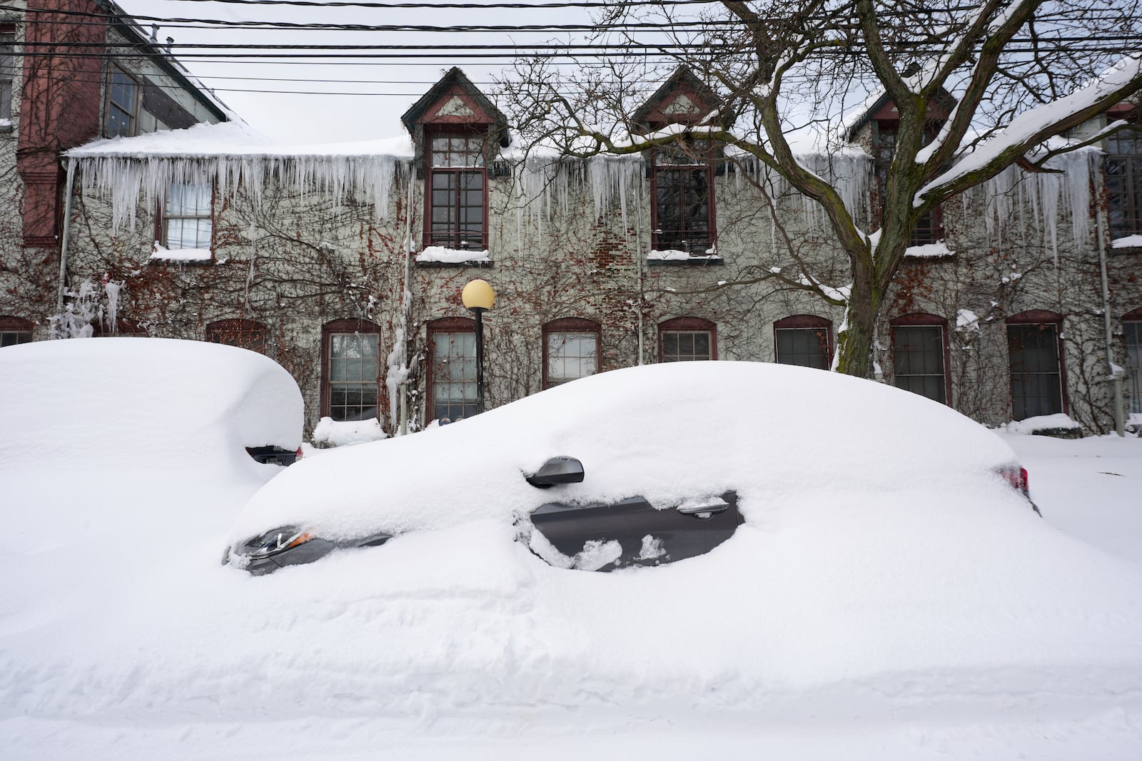 Cars are buried in snow in front of a building with icicles hang from the roof on a side street in downtown Erie, Pa., Tuesday, Nov. 5, 2024. (AP Photo/Gene J. Puskar)