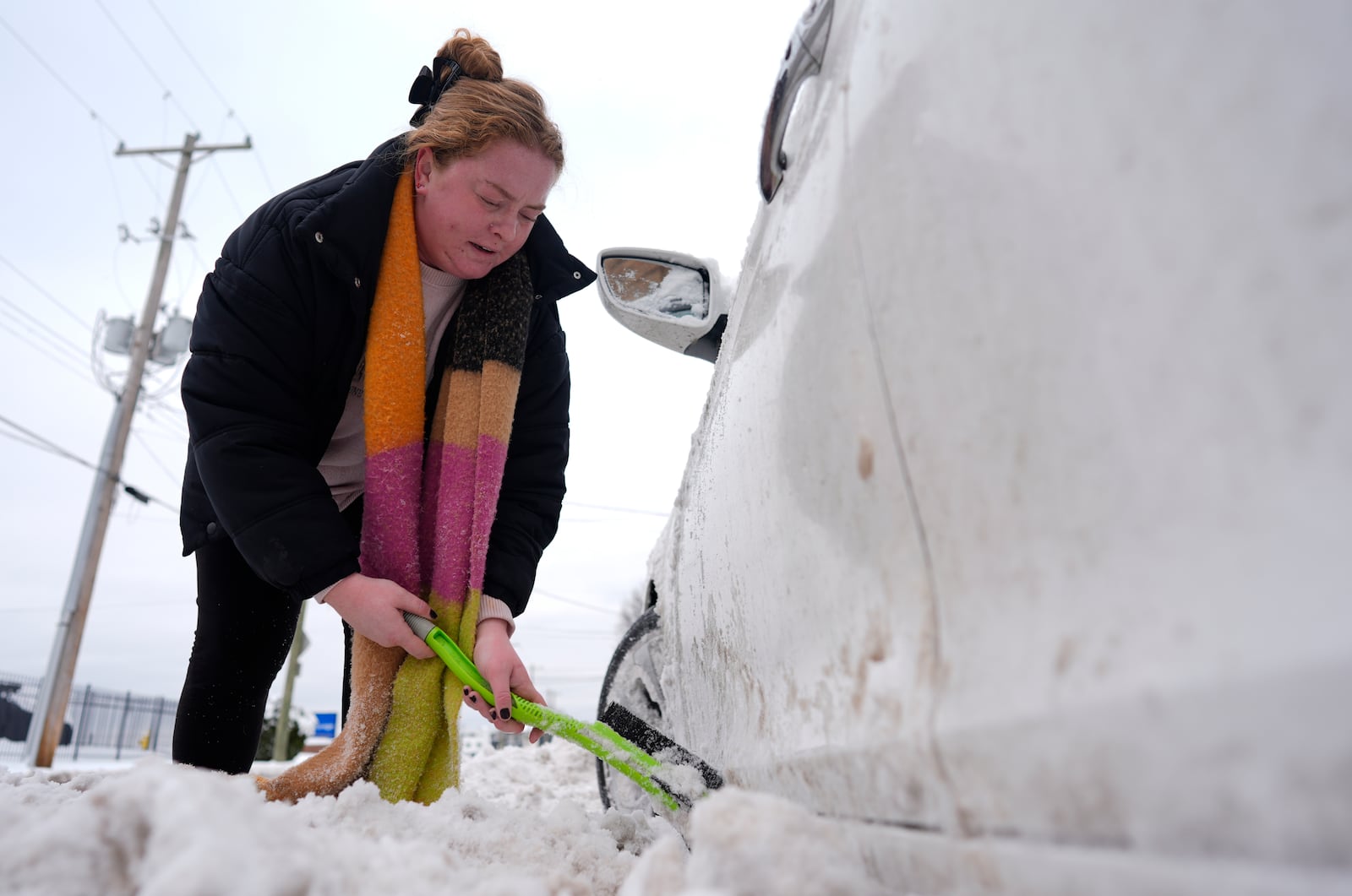 Taylor Mcilwain uses a snow brush to clear snow from around her car in Cincinnati, Tuesday, Jan. 7, 2025. (AP Photo/Carolyn Kaster)