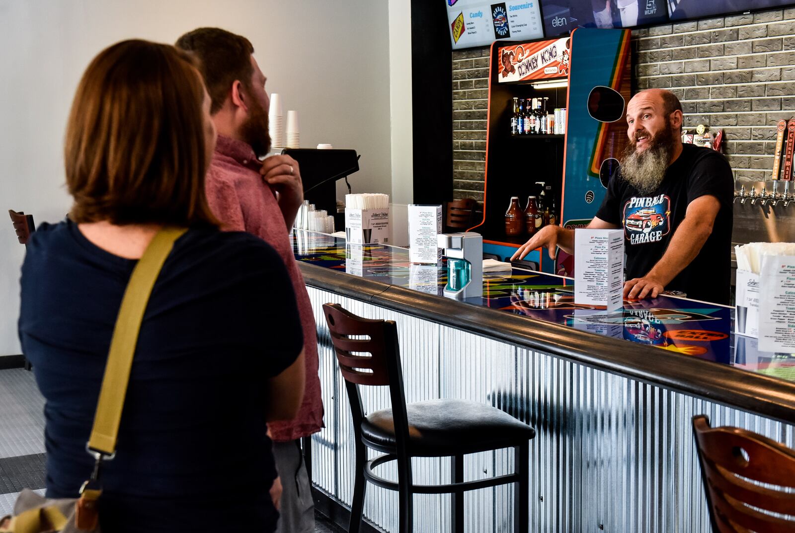 Pinball Garage owner Brad Baker, right, talks to customers Corey and Megan Wagonfield during their visit Thursday, June 25, 2020. Pinball Garage is now open in downtown Hamilton and offers a large selection of pinball machines to play along with a bar with rotating beer selection. NICK GRAHAM / STAFF