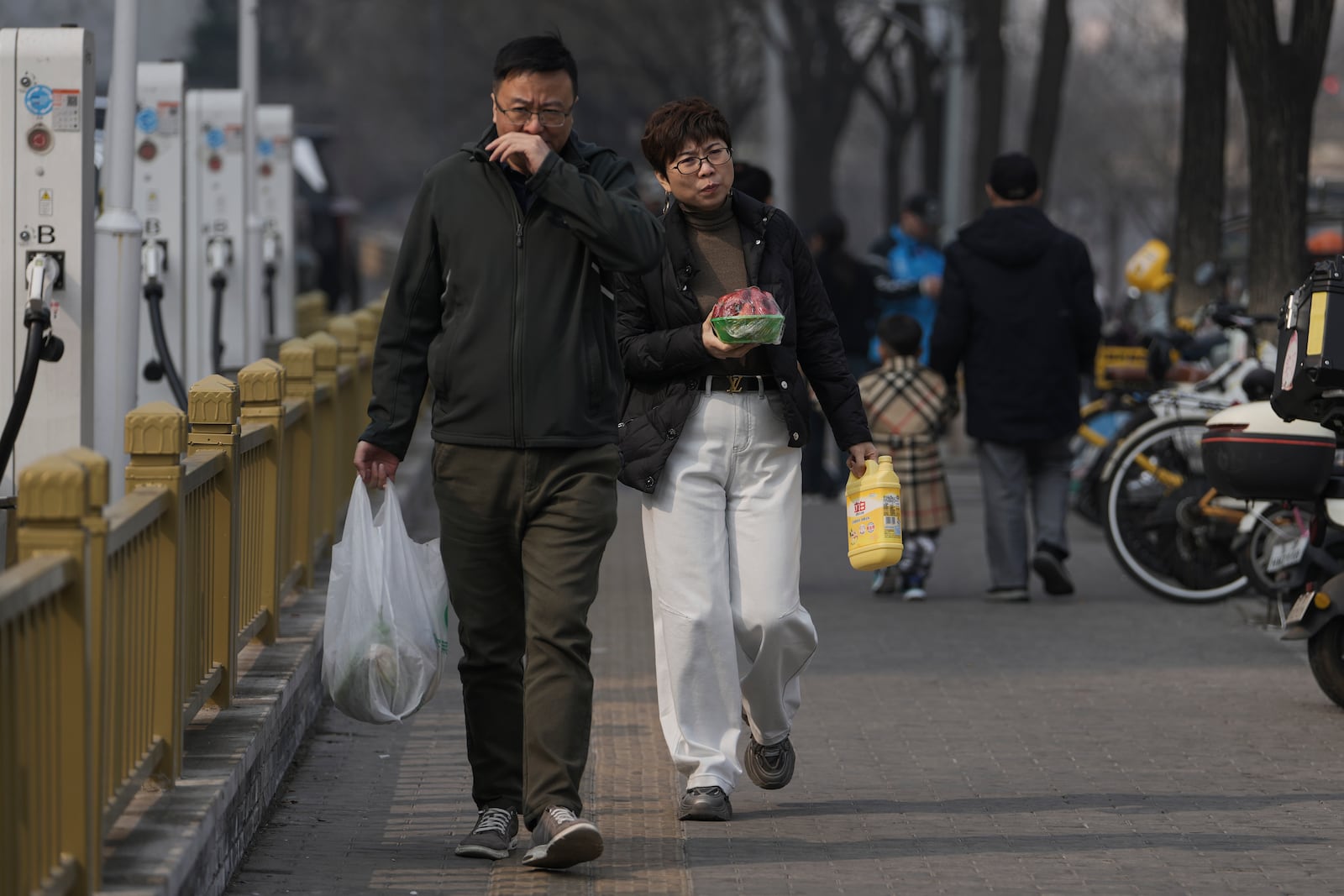 Residents walk with their daily groceries bought from a supermarket in Beijing, Sunday, March 9, 2025. (AP Photo/Andy Wong)