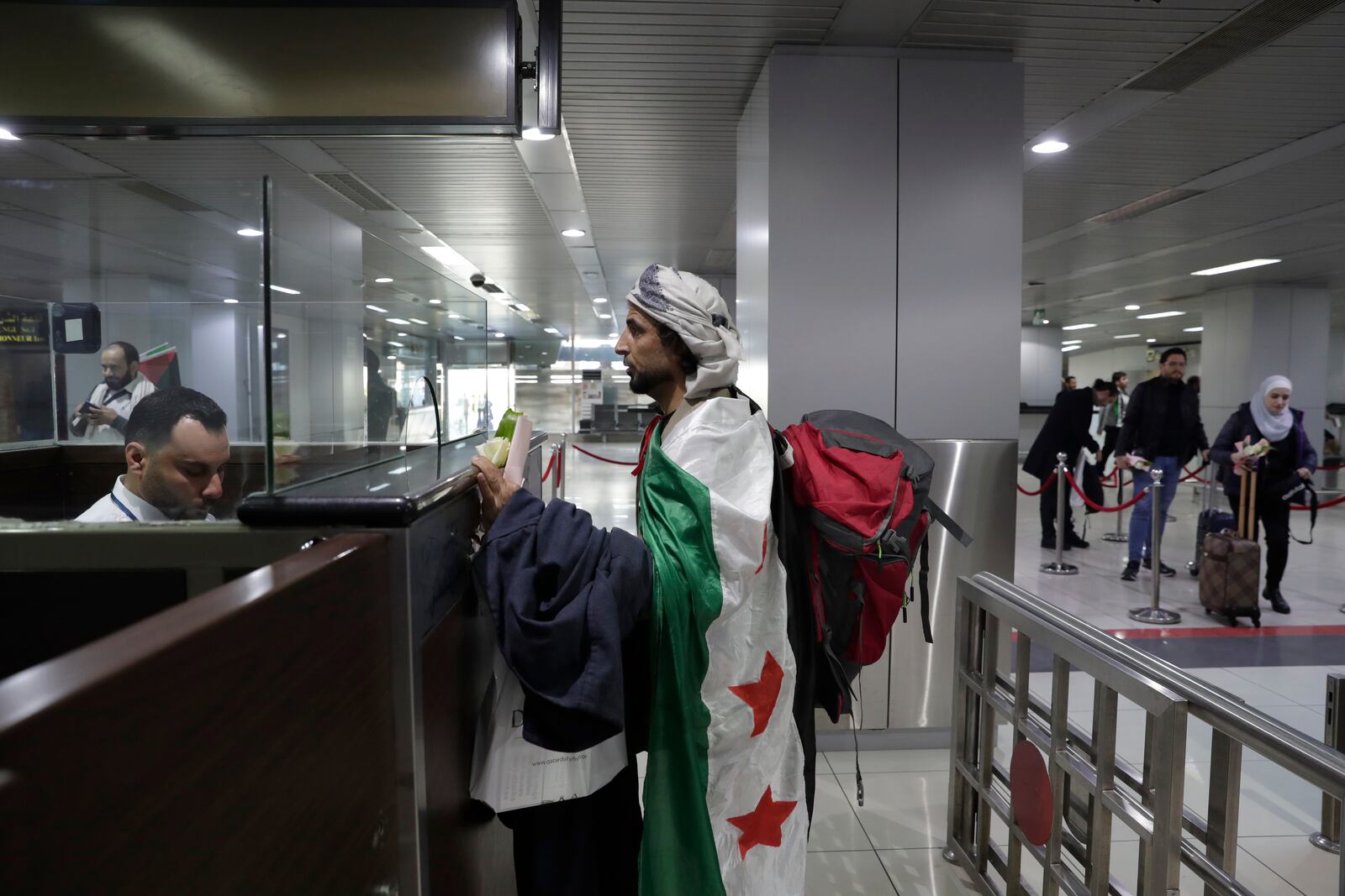 A man who arrived at a first international commercial flight since the fall of former Syrian President Bashar Assad, covers himself with the Syrian "Revolutionary" flag as he checks in at the arrival terminal of Damascus international airport, in Damascus, Syria, Tuesday, Jan. 7, 2025. (AP Photo/Omar Sanadiki)