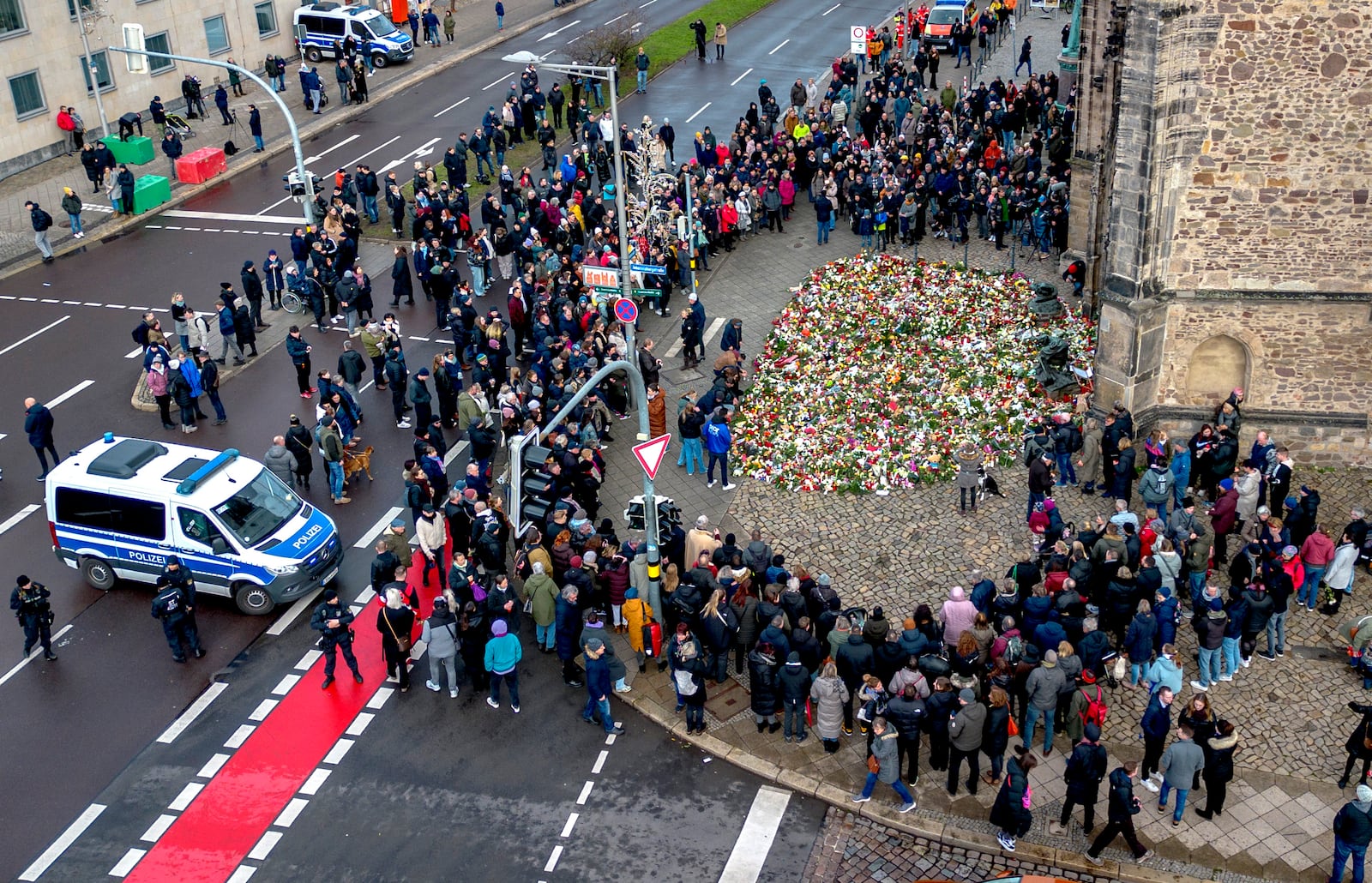 People gather to lay flowers and light candles at the entrance of Johannis church near the Christmas Market, where a car drove into a crowd on Friday evening, in Magdeburg, Germany, Sunday, Dec. 22, 2024. (AP Photo/Michael Probst)