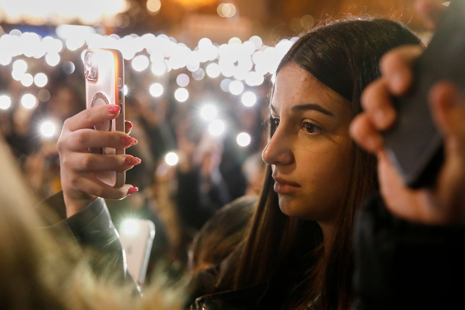 A protester holds her mobile phone as thousands gather for the victims of a massive nightclub fire in the town of Kocani, in Skopje, North Macedonia, Tuesday, March 18, 2025. (AP Photo/Boris Grdanoski)