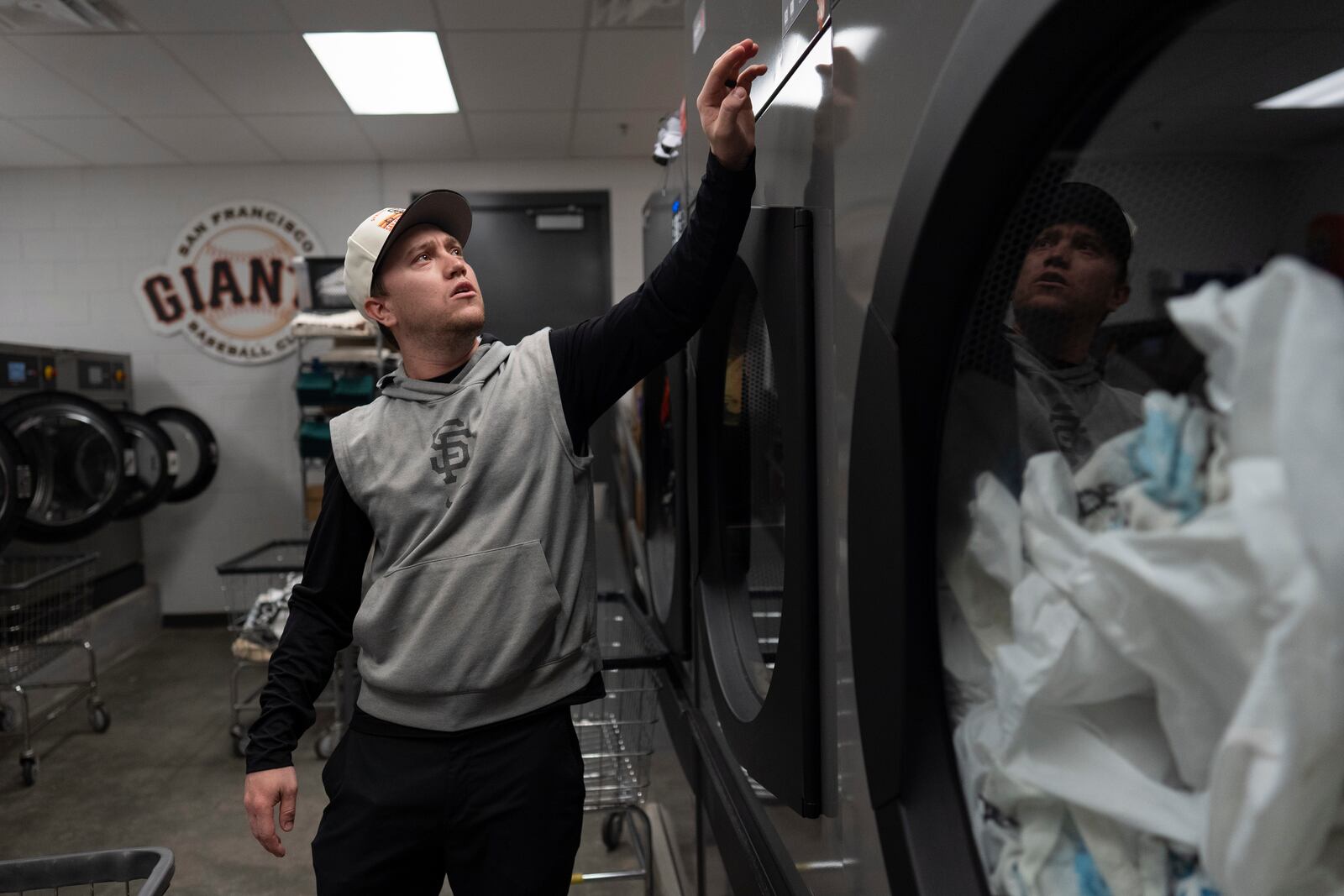 San Francisco Giants clubhouse attendant Riley Halpin starts a clothes dryer in the laundry room during baseball spring training at the team's facility, Monday, Feb. 17, 2025, in Scottsdale, Ariz. (AP Photo/Carolyn Kaster)