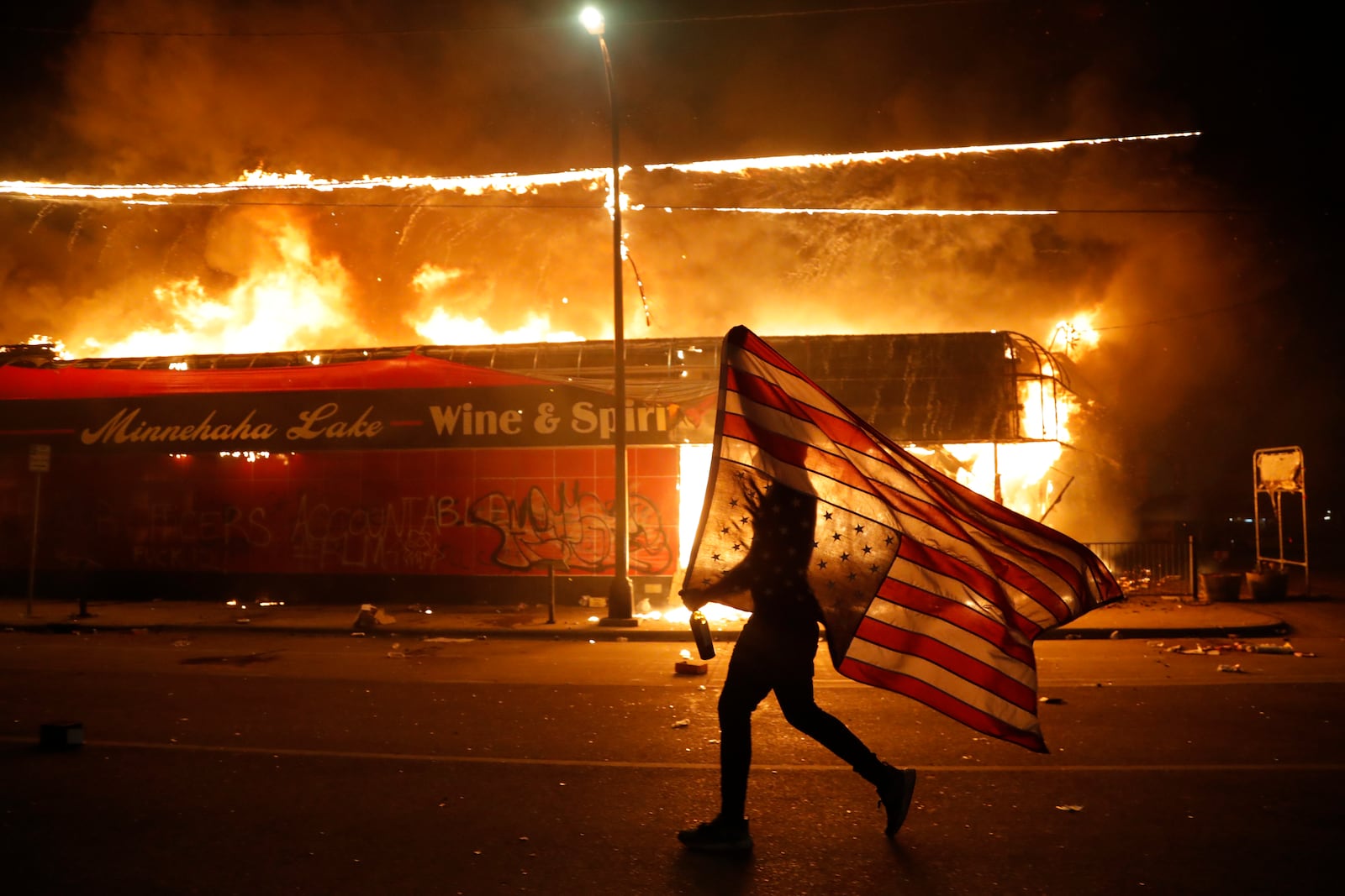 FILE - A protester carries a U.S. flag upside down, a sign of distress, next to a burning building on May 28, 2020, in Minneapolis. (AP Photo/Julio Cortez, File)