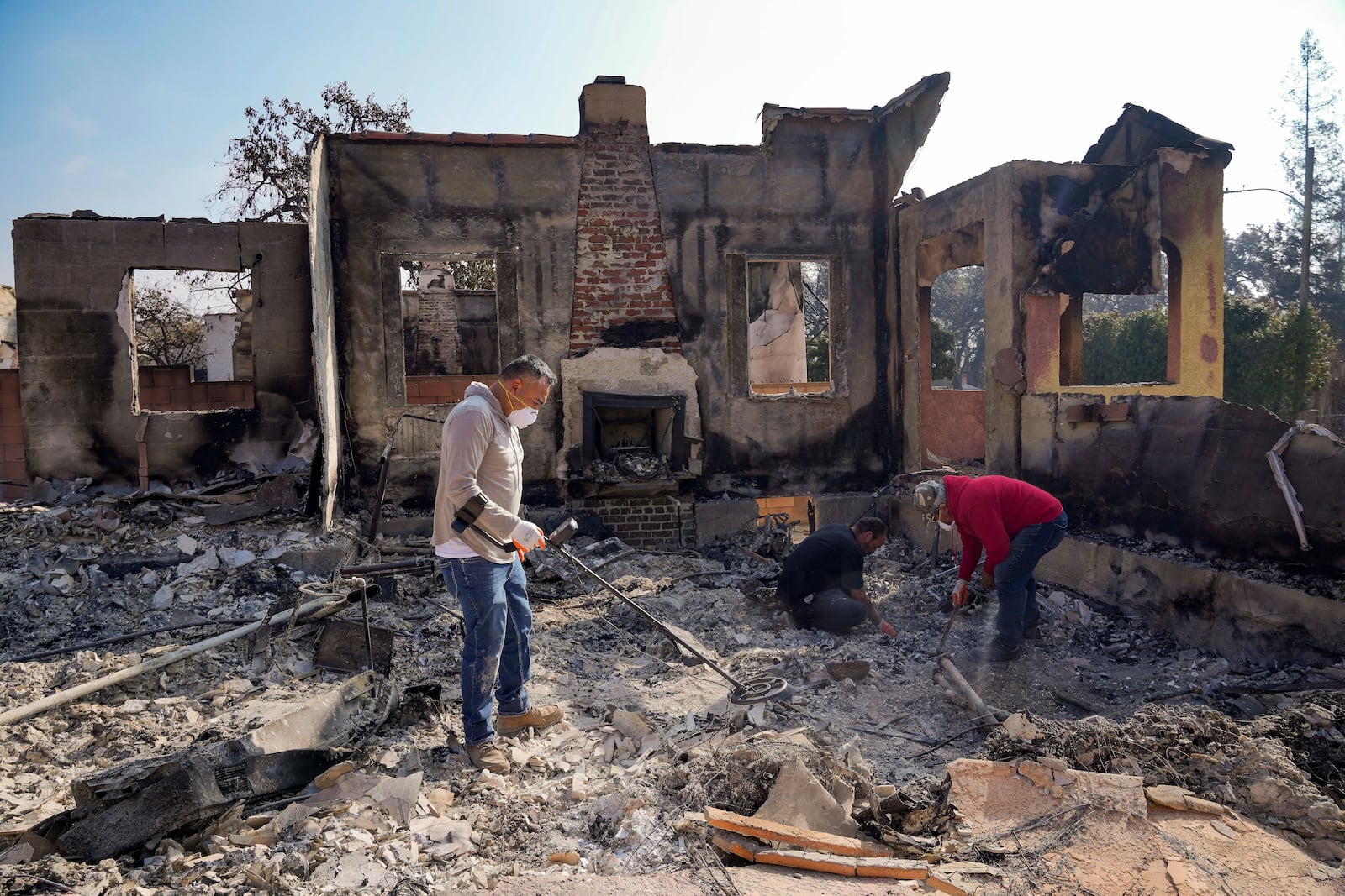 Homeowner David Marquez, left, holds a metal detector as his father, Juan Pablo Alvarado, right, and a friend look for the remains of gold jewelry and other silver items inside the walls of their multi-generational home in the aftermath of the Eaton Fire, Sunday, Jan. 19, 2025, in Altadena, Calif. (AP Photo/Damian Dovarganes)