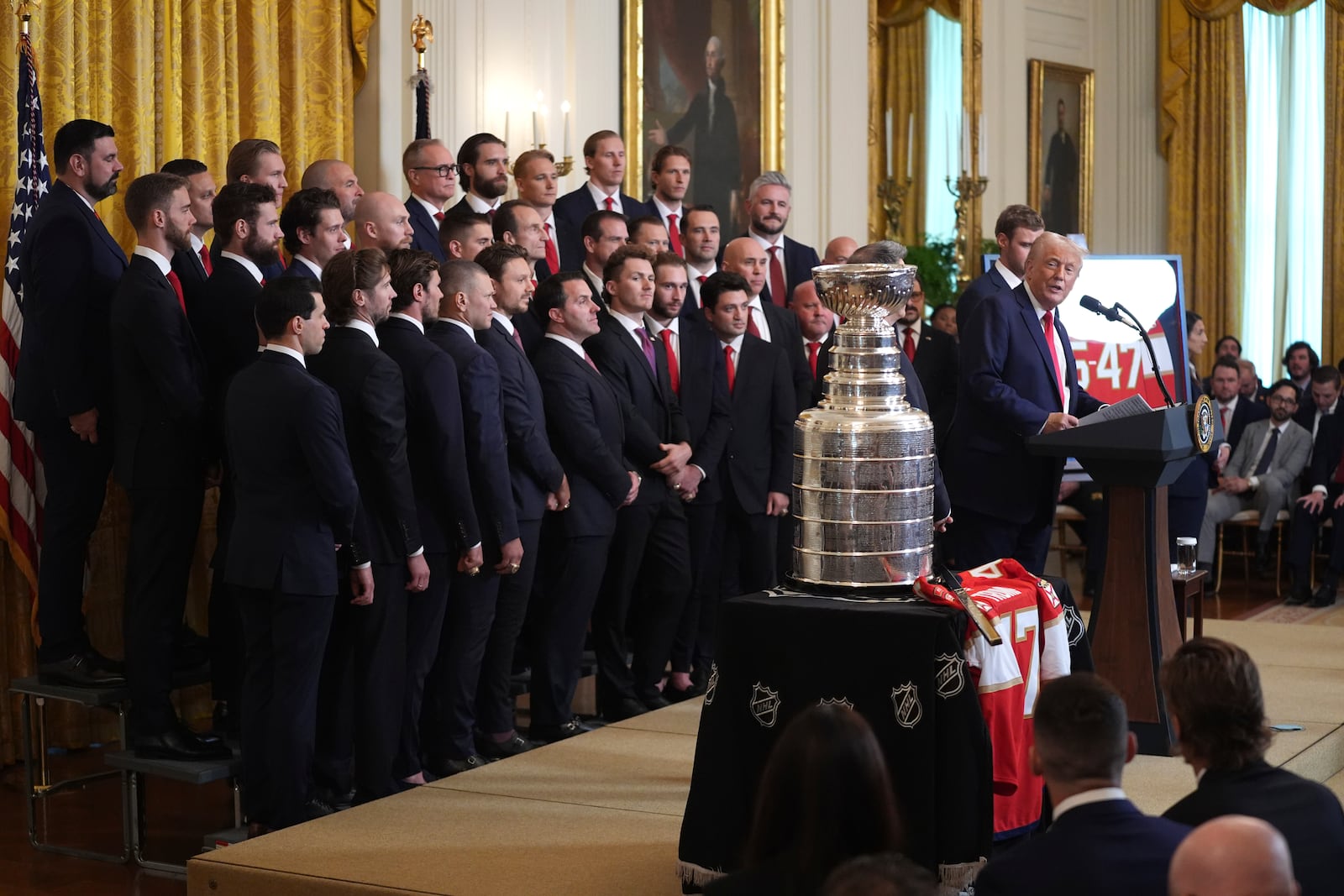 President Donald Trump speaks during an event to honor the 2024 NHL Stanley Cup champion Florida Panthers hockey team, pictured at left, in the East Room of the White House, Monday, Feb. 3, 2025, in Washington. (AP Photo/Evan Vucci)