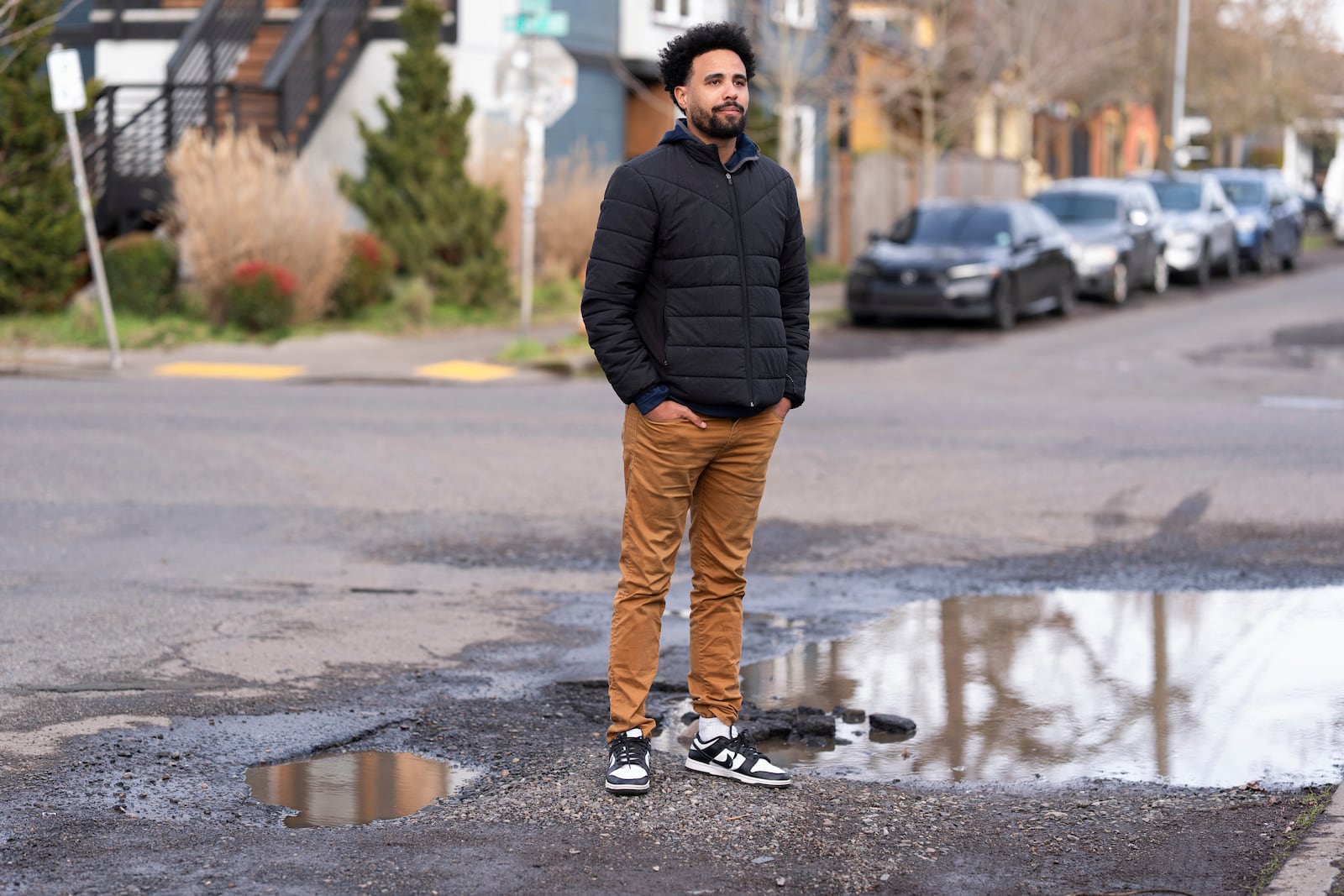 Timothy Taylor poses for a photo by pot holes outside his home on Thursday, Feb. 6, 2025, in Portland, Ore. Taylor said a pot hole broke part of his car's suspension and cost him $1,000 to fix. (AP Photo/Jenny Kane)