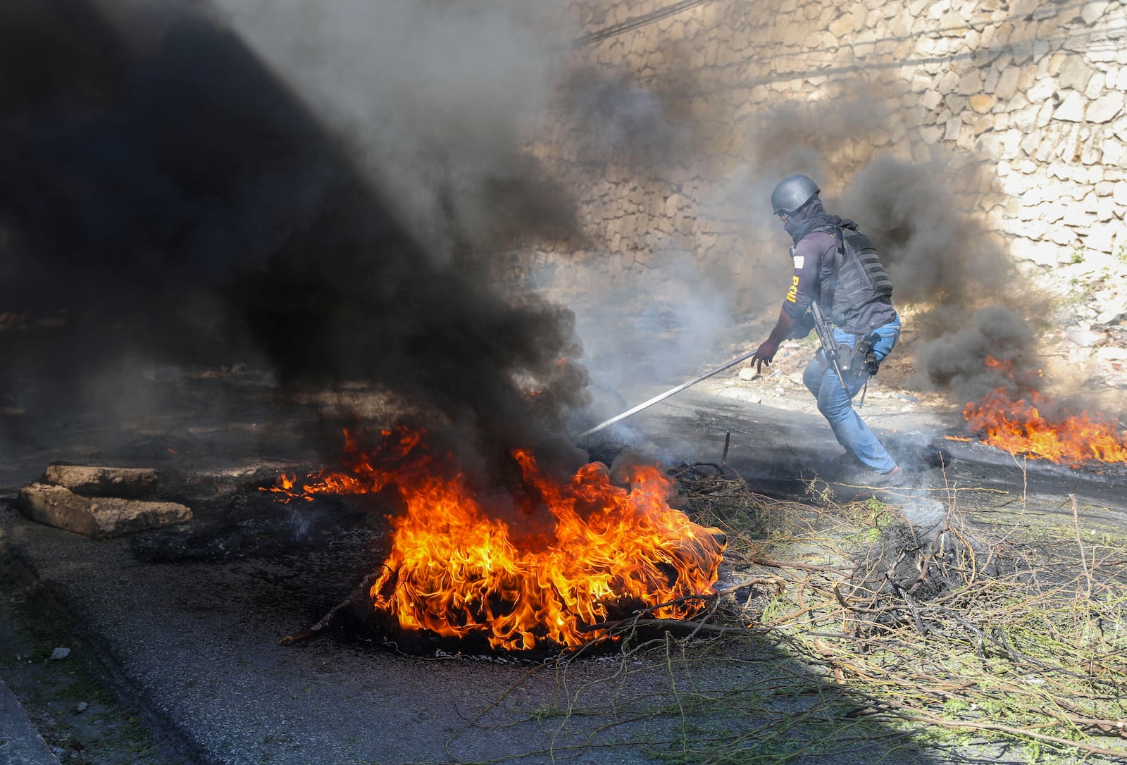 A police officer works to clear barricades of burning tires set on fire by residents to deter gang members from entering their neighborhood, in Port-au-Prince, Haiti, Tuesday, Nov. 19, 2024. (AP Photo/Odelyn Joseph)