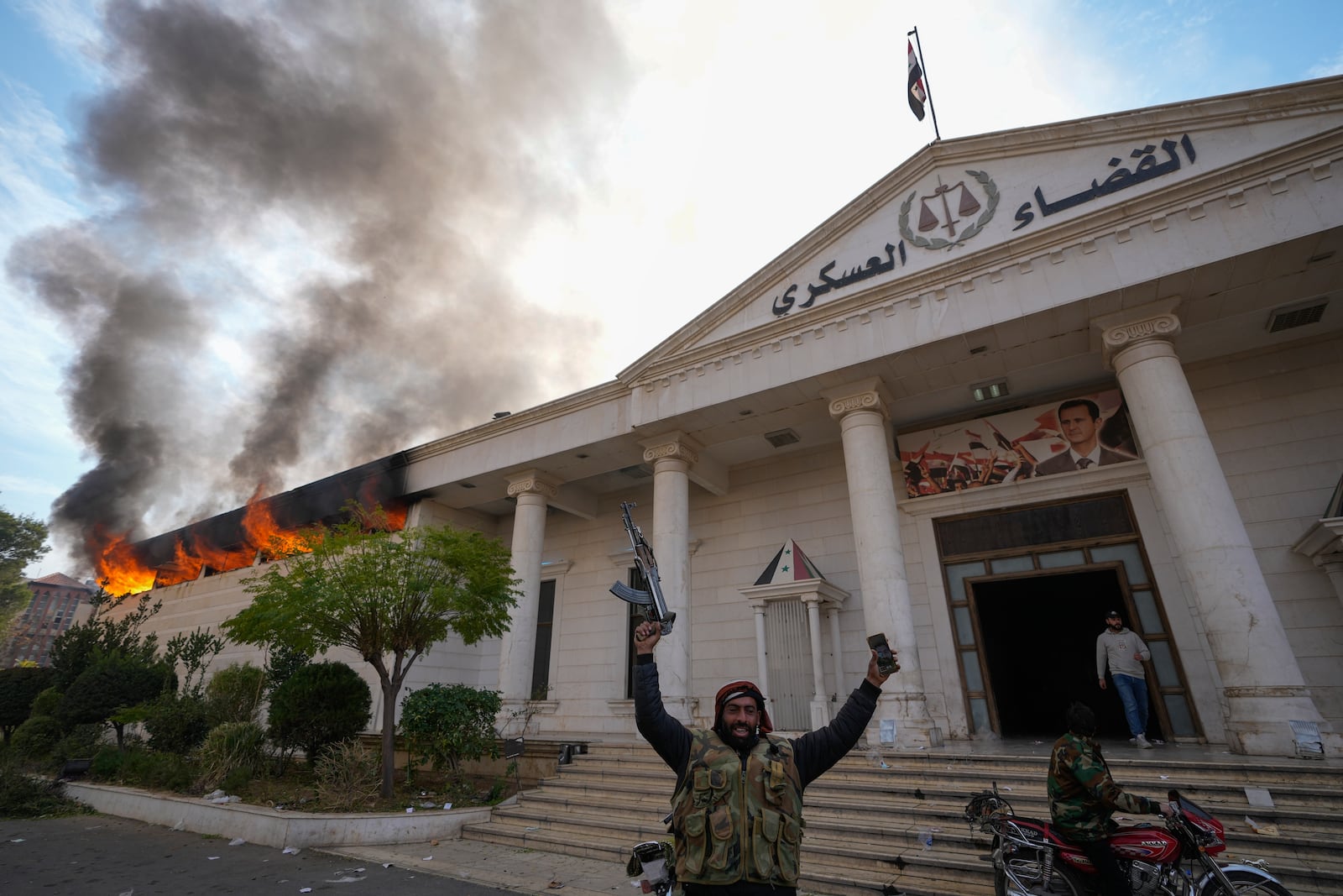 FILE - Opposition fighters celebrate as a military court burns in Damascus, Syria, on Sunday, Dec. 8, 2024. (AP Photo/Hussein Malla, File)