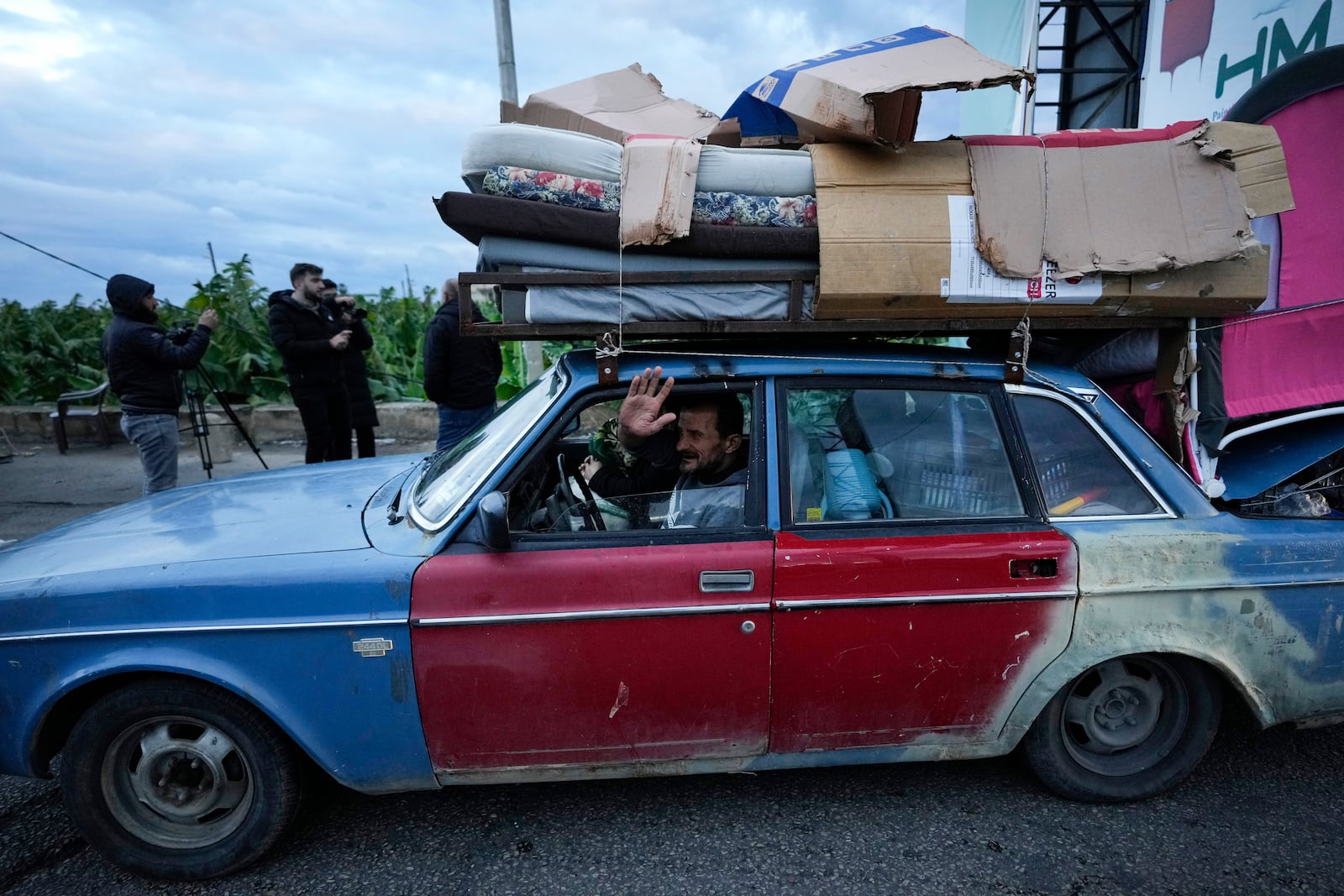 A man who is returning to his village waves as he carries his belongings on his car after the ceasefire between Hezbollah and Israel began early morning, in Tyre, south Lebanon, Wednesday, Nov. 27, 2024. (AP Photo/Hussein Malla)