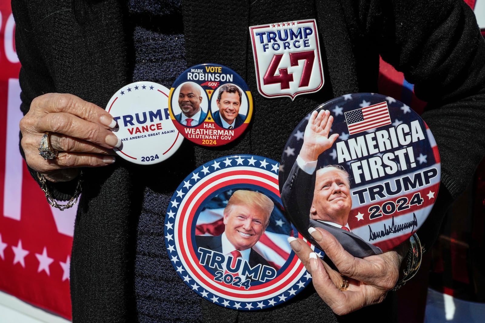 Ann McDonald of Rutherfordton, shows off her display of political buttons in support of the Republican ticket, former President Trump, Lt. Gov. Mark Robinson and Hal Weatherman, Thursday, Oct. 17, 2024, outside the Rutherford County Annex Building on the first day of early voting, in Rutherfordton, N.C. (AP Photo/Kathy Kmonicek)