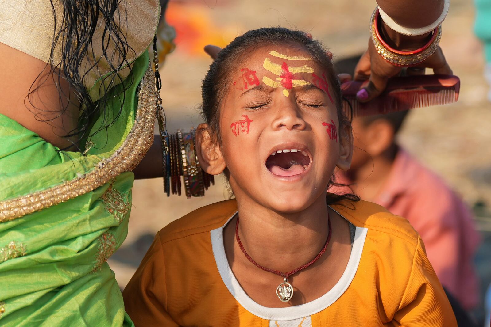 A young Hindu devotee, marked with sacred symbols on her face, reacts as her mother combs her hair at the confluence of the Ganges, the Yamuna, and the Saraswati rivers during the 45-day-long Maha Kumbh festival in Prayagraj, India, Tuesday, Jan. 28, 2025. (AP Photo/Deepak Sharma)