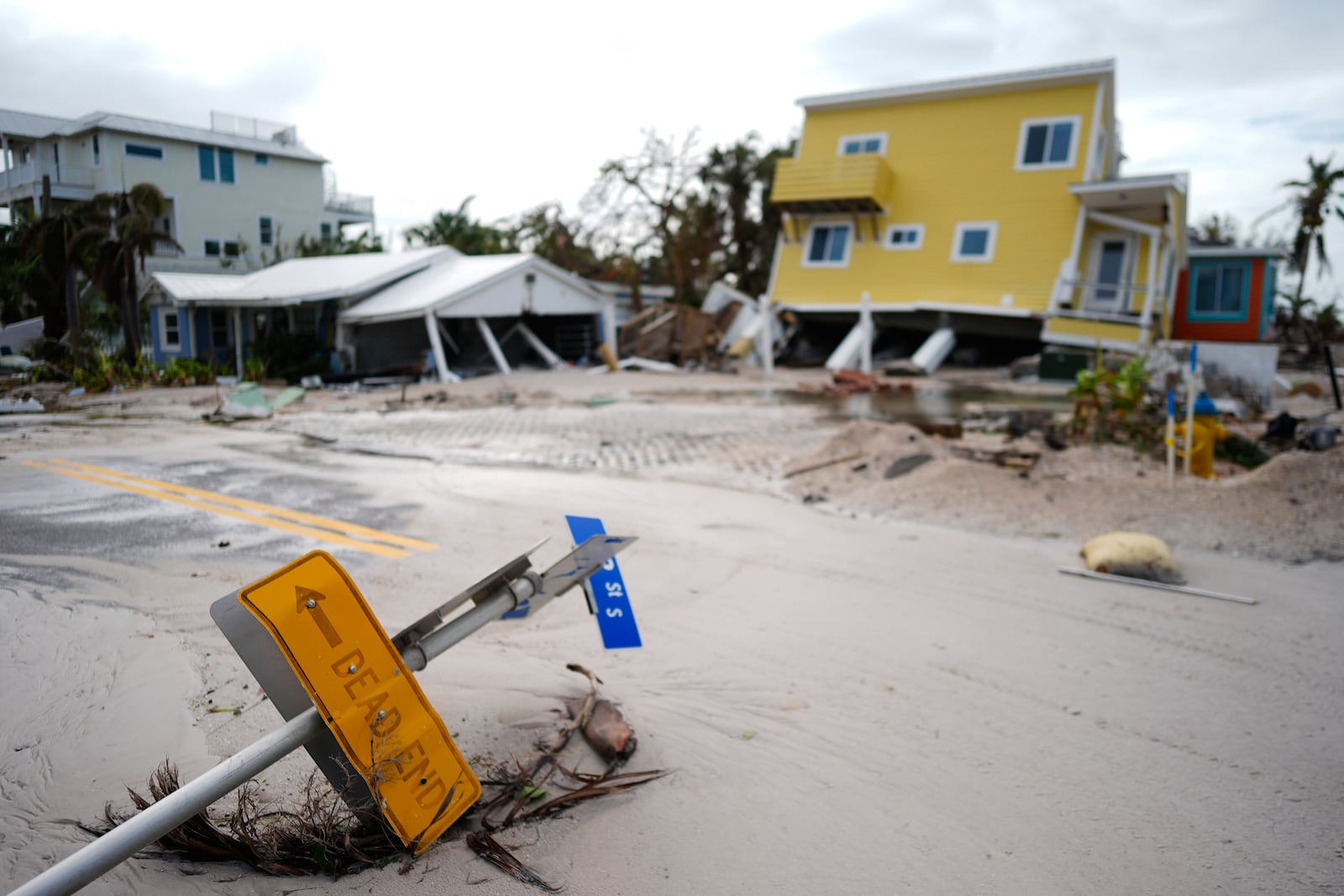 A house, top right, sits toppled off its stilts after the passage of Hurricane Milton, alongside an empty lot where a home was swept away by Hurricane Helene, in Bradenton Beach on Anna Maria Island, Fla., Thursday, Oct. 10, 2024. (AP Photo/Rebecca Blackwell)