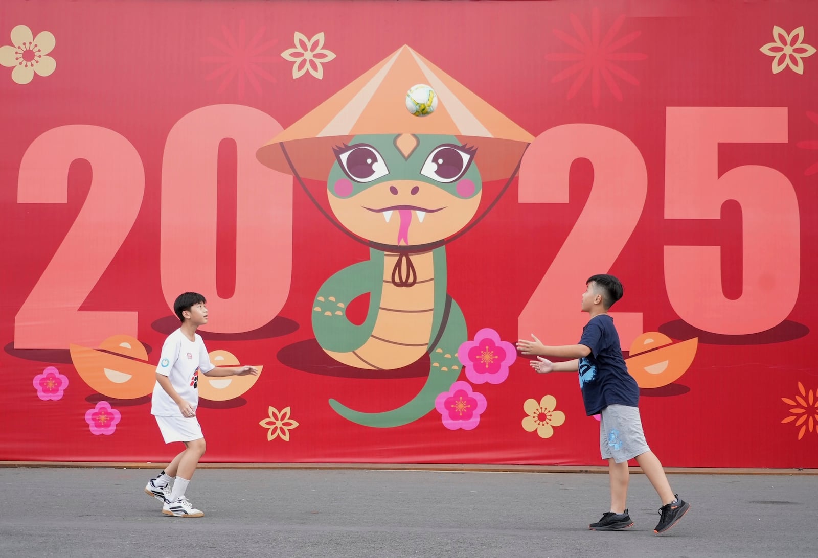 Two boys play football in front of a billboard welcoming the New Year 2025 in Ho Chi Minh city, Vietnam on Tuesday, Dec.31, 2024. (AP Photo/Hau Dinh)