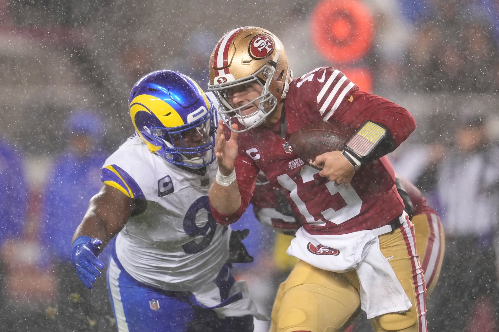 Rain falls as San Francisco 49ers quarterback Brock Purdy (13) tries to scramble before being sacked by Los Angeles Rams defensive tackle Kobie Turner, left, during the first half of an NFL football game in Santa Clara, Calif., Thursday, Dec. 12, 2024. (AP Photo/Godofredo A. Vásquez)