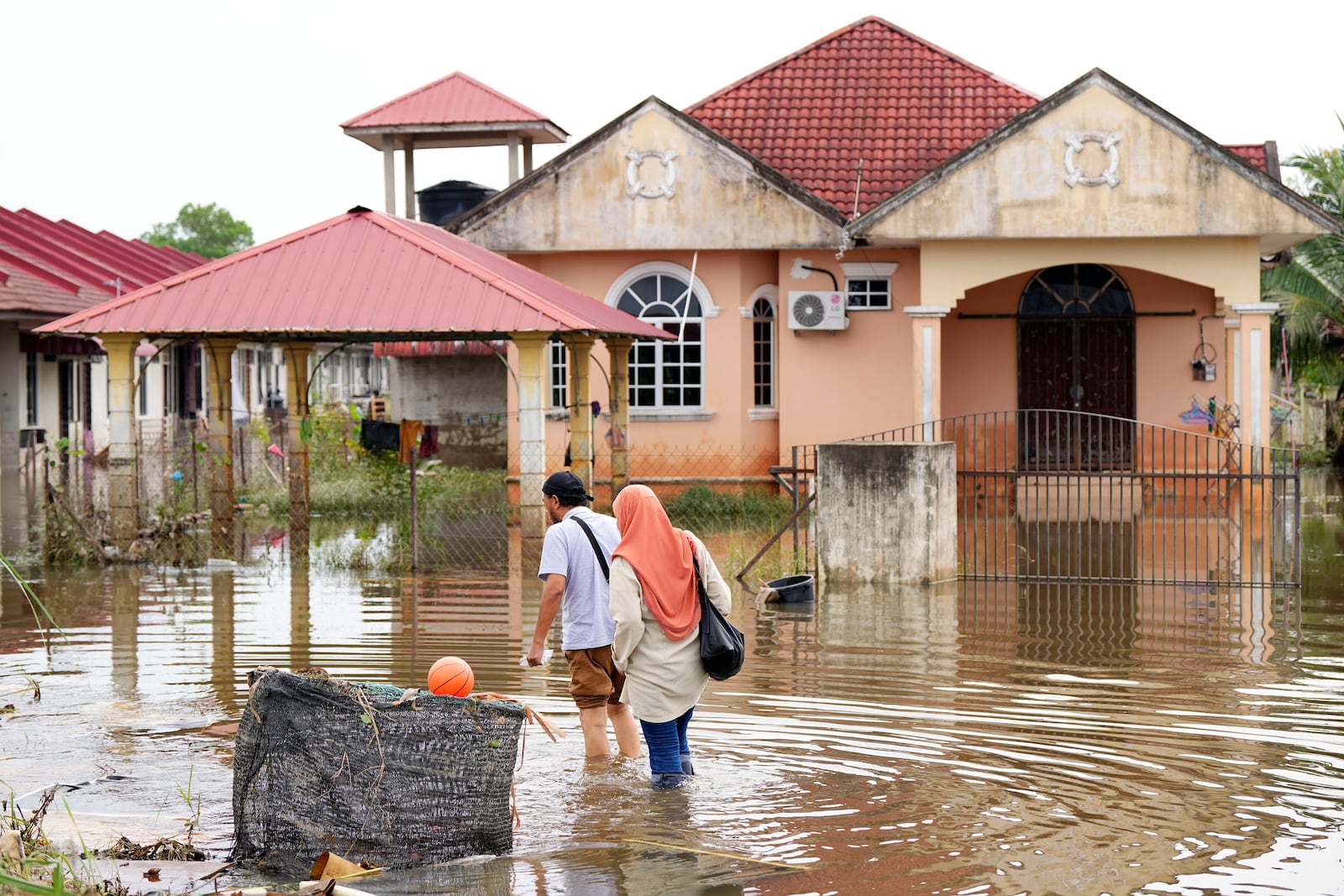 People wade through the water at a neighborhood affected by a flood in Tumpat, on the outskirts of Kota Bahru, Malaysia, Tuesday, Dec. 3, 2024. (AP Photo/Vincent Thian)