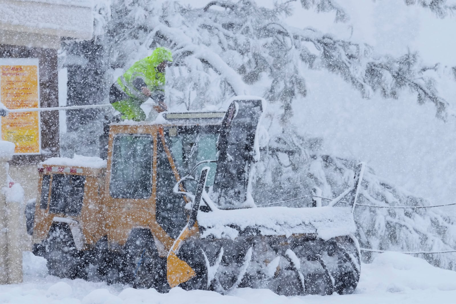 A person kneels on top of a plow tractor during a storm Thursday, Feb. 13, 2025, in Truckee, Calif. (AP Photo/Brooke Hess-Homeier)