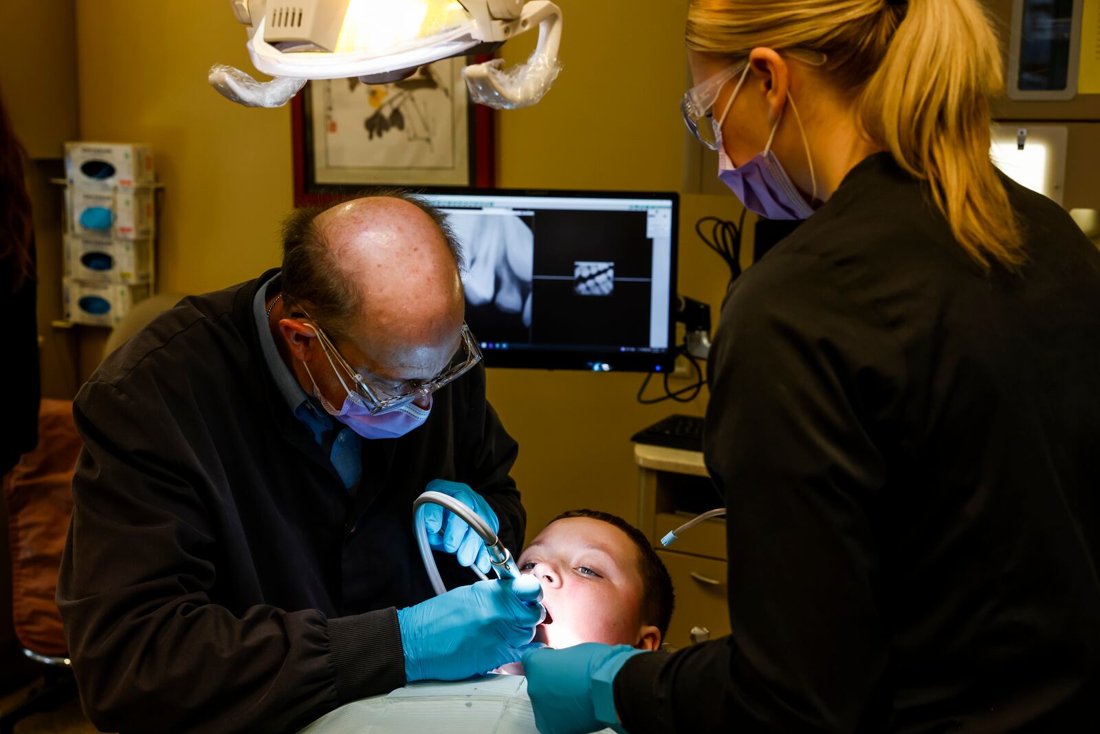 Gabe Blue, a student from Middletown's Rosa Parks Elementary, gets an exam by dentist Mike Vorherr, left, as Butler Tech Dental Science student Elaina Hulley looks on Friday, Feb. 9, 2024 during the "Give Kids A Smile" kickoff event at Butler Tech Bioscience Center in West Chester Township. 
  The event featured volunteer dentists and Dental Science students from Butler Tech, who provided critical dental services to approximately 30 fifth-grade students from Rosa Parks Elementary School in Middletown. NICK GRAHAM/STAFF