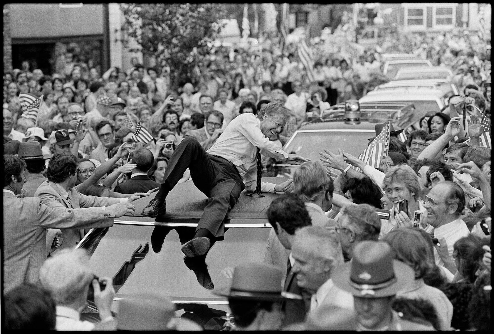 FILE - President Jimmy Carter leans across the roof of his car to shake hands along the parade route through Bardstown, Ky., July 31, 1979. The president climbed on top of the car as the parade moved toward the high school gym, where a town meeting was held. (AP Photo/Bob Daugherty, File)