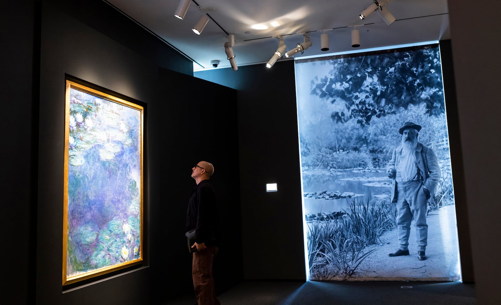 A man looks at "Nympheas," left, by artist Claude Monet, in photo on right, during an auction preview at Sotheby's in New York, Monday, Nov. 11, 2024. (AP Photo/Eduardo Munoz Alvarez)