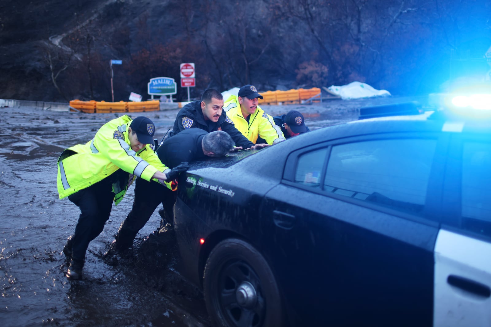 Police officers push an emergency vehicle stuck in mud in the Palisades Fire zone during a storm Thursday, Feb. 13, 2025, in Malibu, Calif. (AP Photo/Ethan Swope)