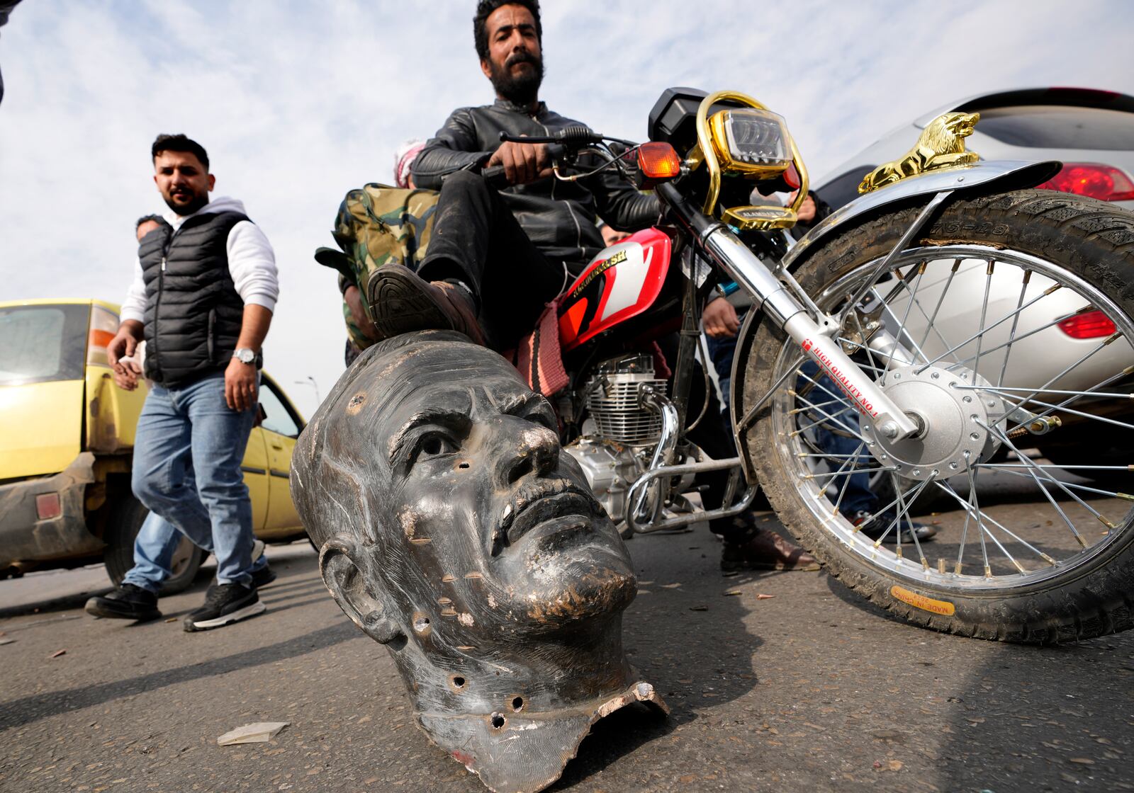 FILE - An opposition fighter riding a motorcycle steps on a broken bust of the late Syrian President Hafez Assad, in Damascus, Syria, on Sunday, Dec. 8, 2024. (AP Photo/Hussein Malla, File)