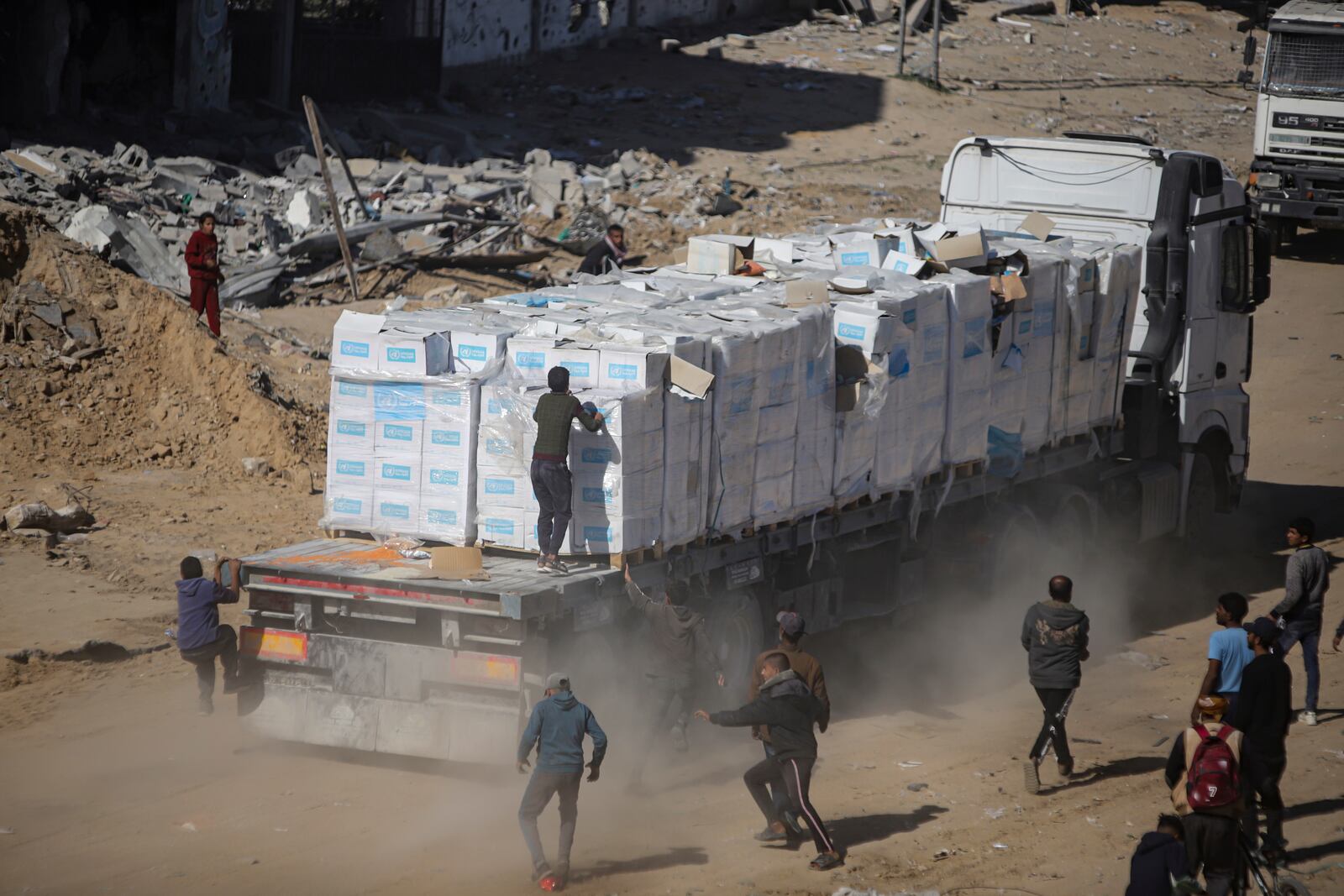 Palestinians chase humanitarian aid trucks that arrived through the Kerem Shalom crossing from Egypt into the Gaza Strip, in Rafah, Tuesday, Jan. 21, 2025. (AP Photo/Jehad Alshrafi)