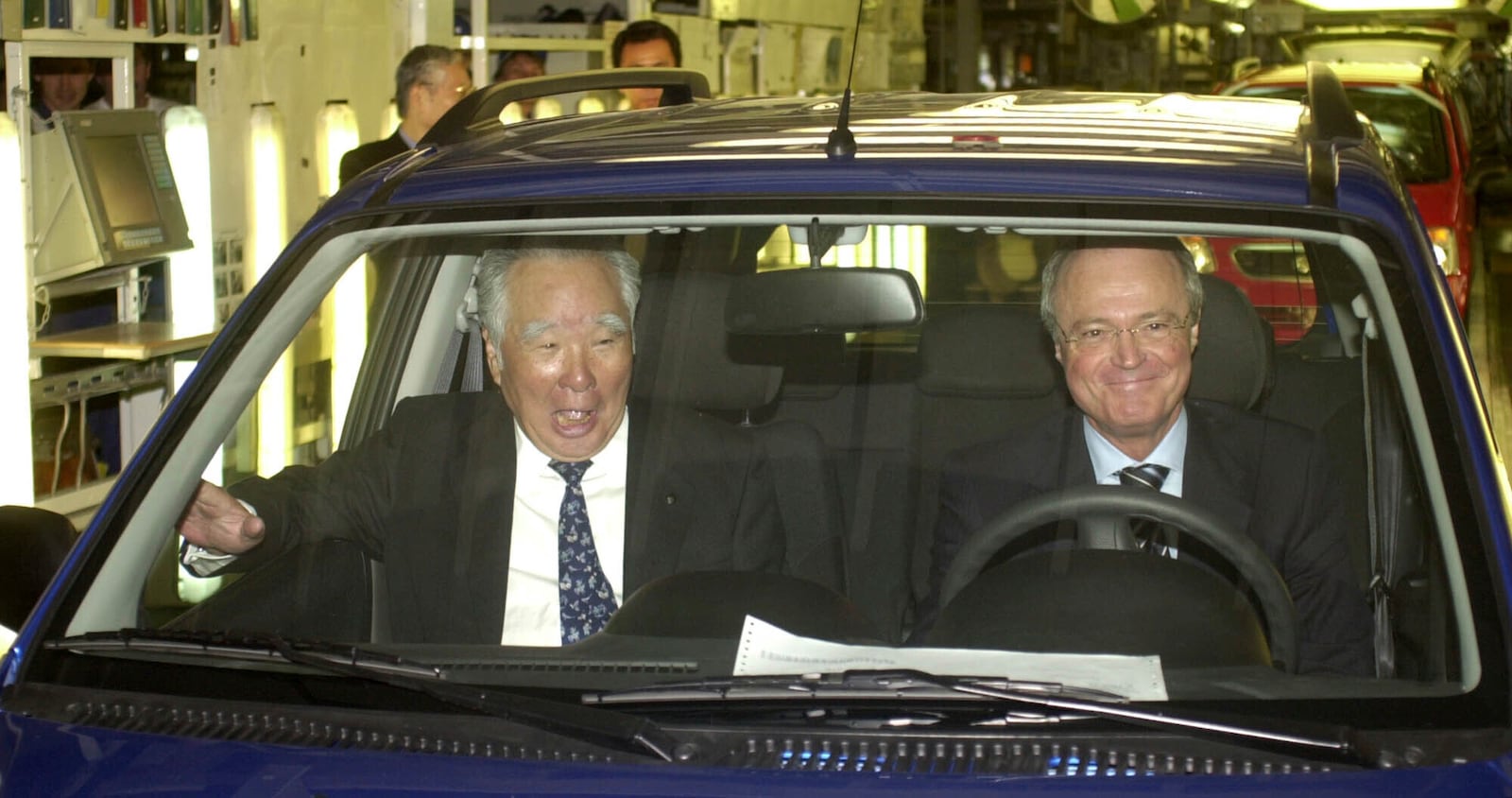 FILE - Osamu Suzuki, head of the Suzuki Motor Corporation, left, sits in the first Suzuki Ignis made in Hungary next to Hungarian Prime Minister Peter Medgyessy just after the production start of the new Suzuki model in Esztergom near Budapest, Hungary, April 10, 2003. (AP Photo/Bela Szandelszky, File)