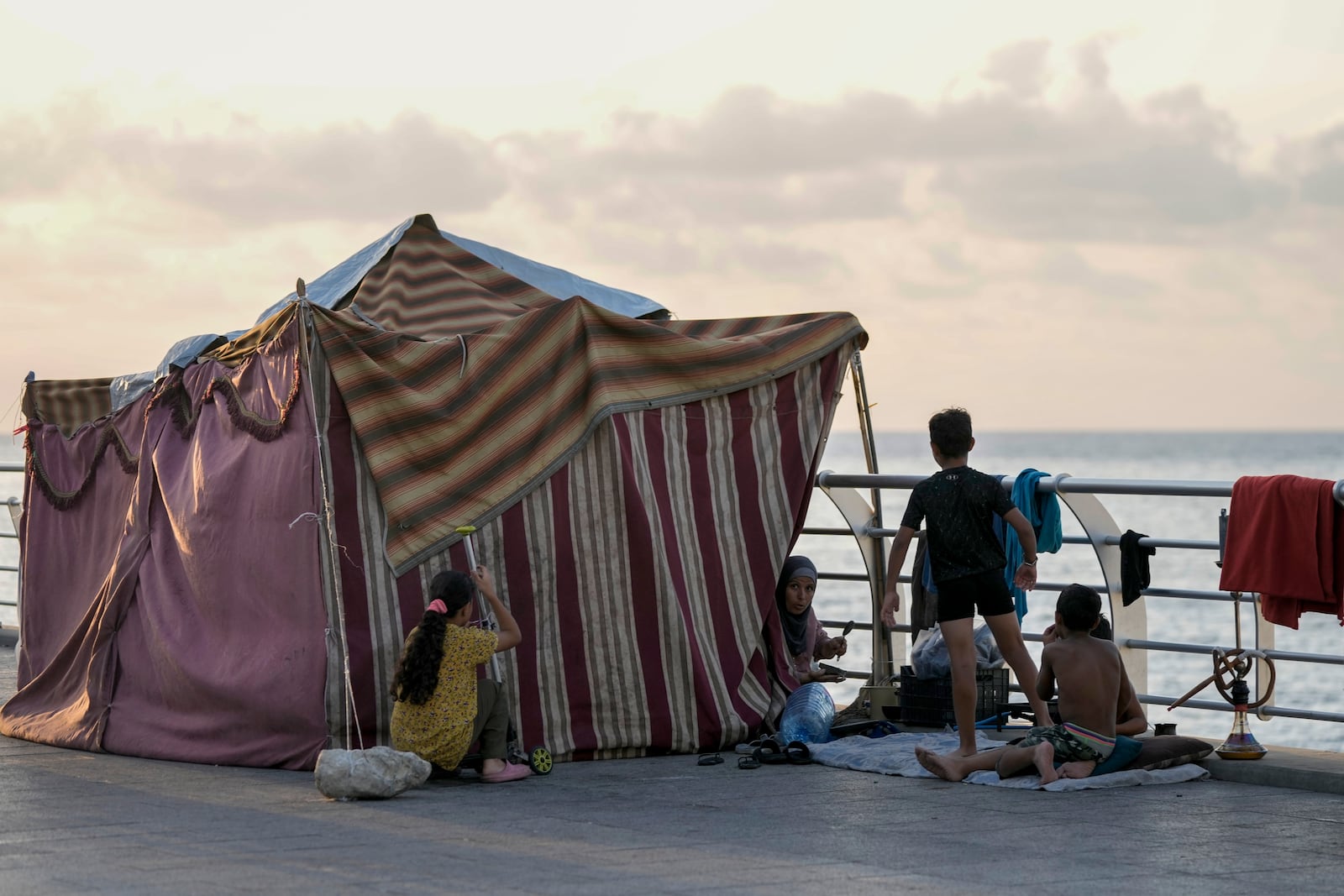 A displaced family fleeing the Israeli airstrikes in the south, sits next to their tent on Beirut's corniche, Lebanon, Monday, Oct. 14, 2024. (AP Photo/Bilal Hussein)