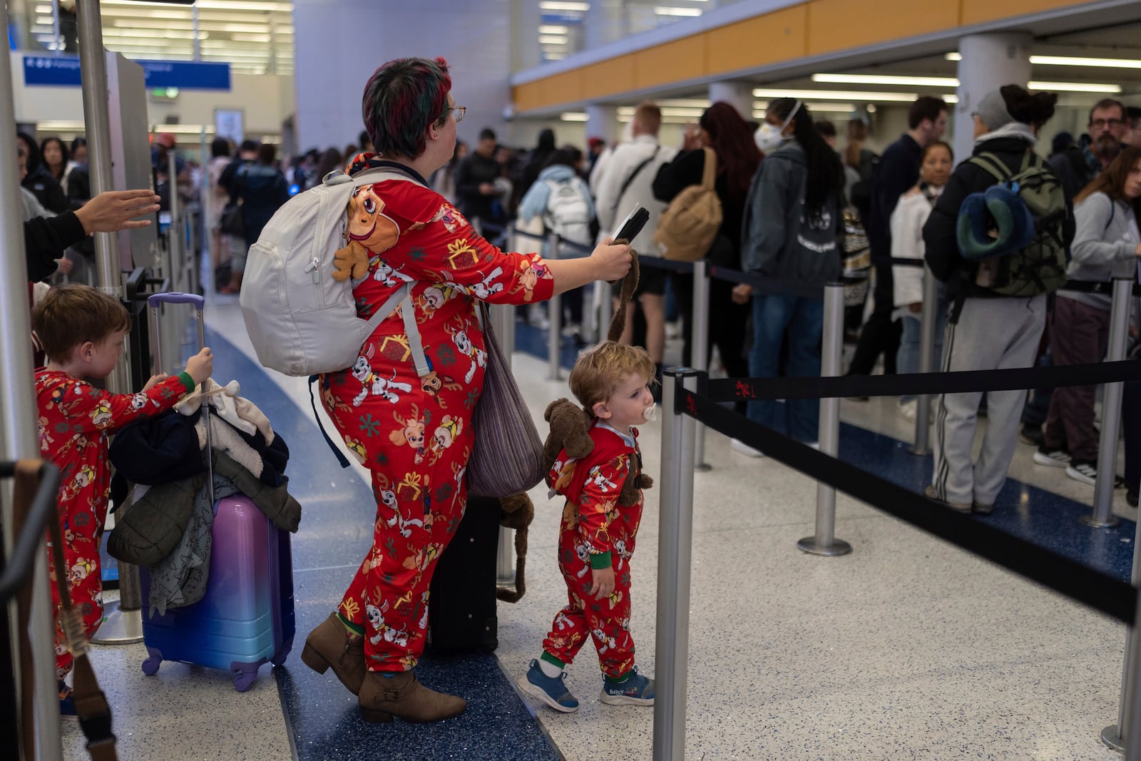 Marie Digna, traveling to Grand Rapids, Mich., enters security with her two sons, Lucian, right, and Samson, at Los Angeles International Airport on Tuesday, Dec. 24, 2024. (AP Photo/Jae C. Hong)