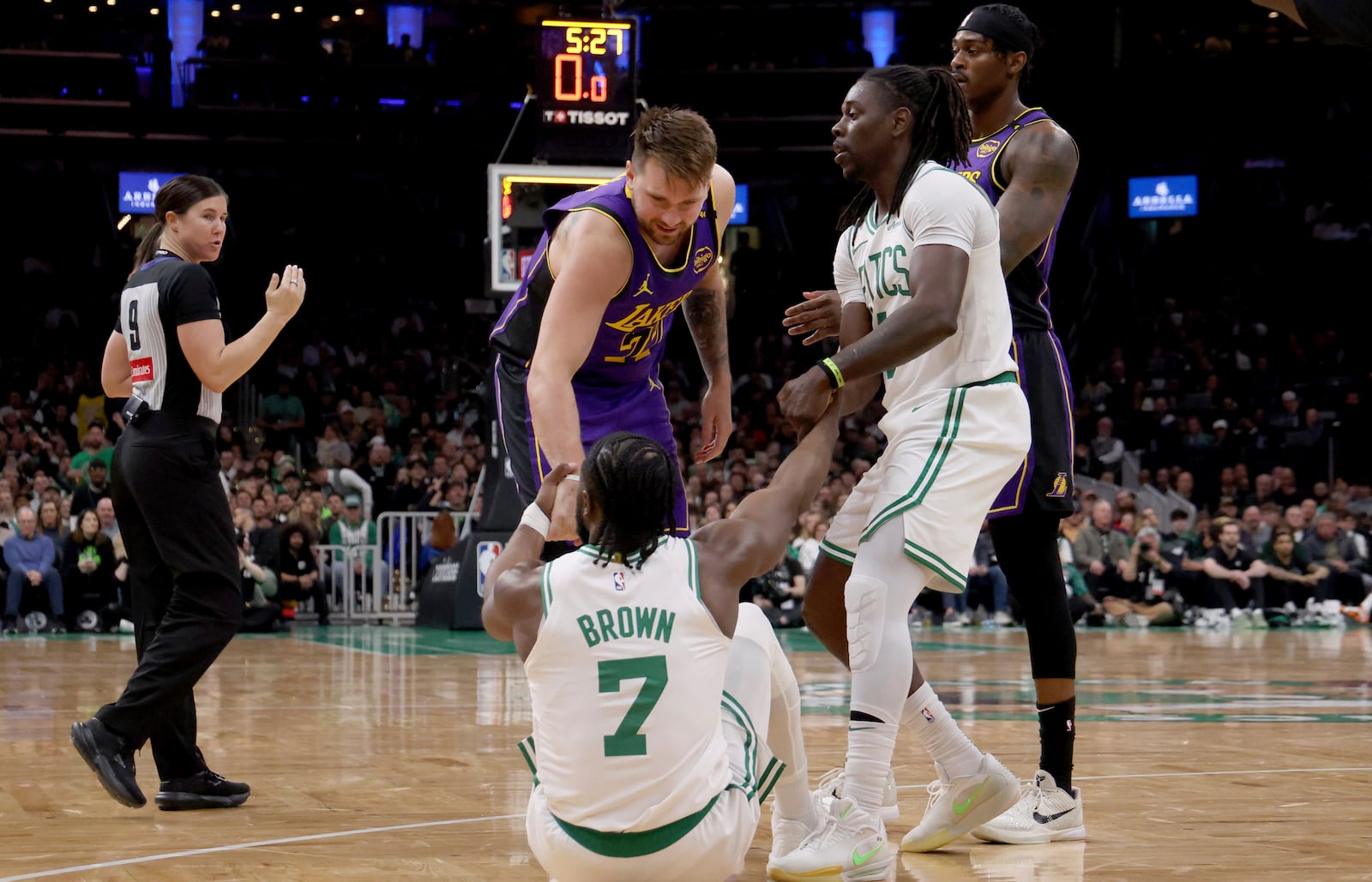 Los Angeles Lakers guard Luka Doncic, left, and Boston Celtics guard Jrue Holiday, right, help Boston Celtics guard Jaylen Brown (7) up after falling to the court during the first half of an NBA basketball game, Saturday, March 8, 2025, in Boston. (AP Photo/Mark Stockwell)