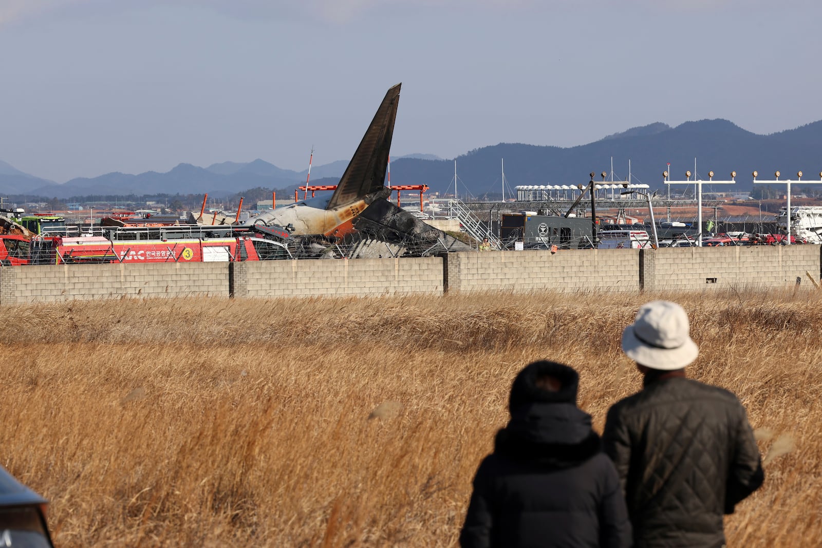 People watch as firefighters and rescue team members work at Muan International Airport in Muan, South Korea, Sunday, Dec. 29, 2024. (Cho Nam-soo/Yonhap via AP)