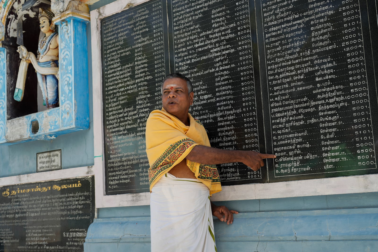 M. Natarajan, head priest of Sri Dharmasastha Hindu temple points out the name of Democratic presidential nominee Vice President Kamala Harris on a plaque, displaying names of donors written in Tamil language who donated for the renovation of temple, in Thulasendrapuram, the ancestral village of Harris, in Tamil Nadu state, India, Monday, Nov. 4, 2024. (AP Photo/Aijaz Rahi)